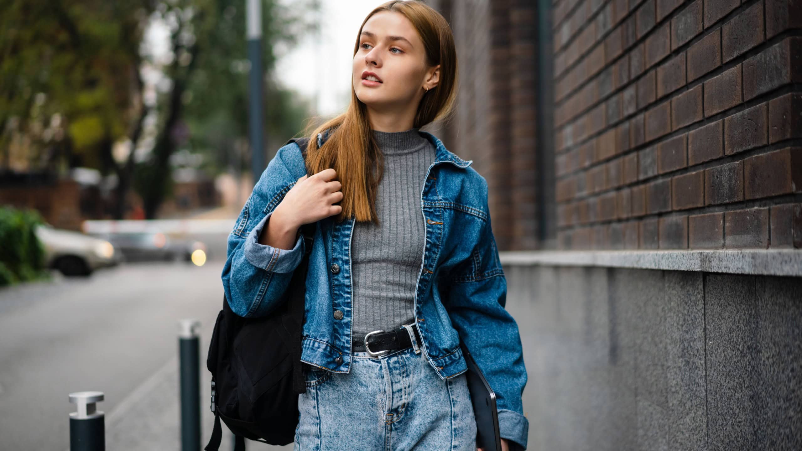 Beautiful young woman wearing denim clothes walking on a street, carrying laptop computer