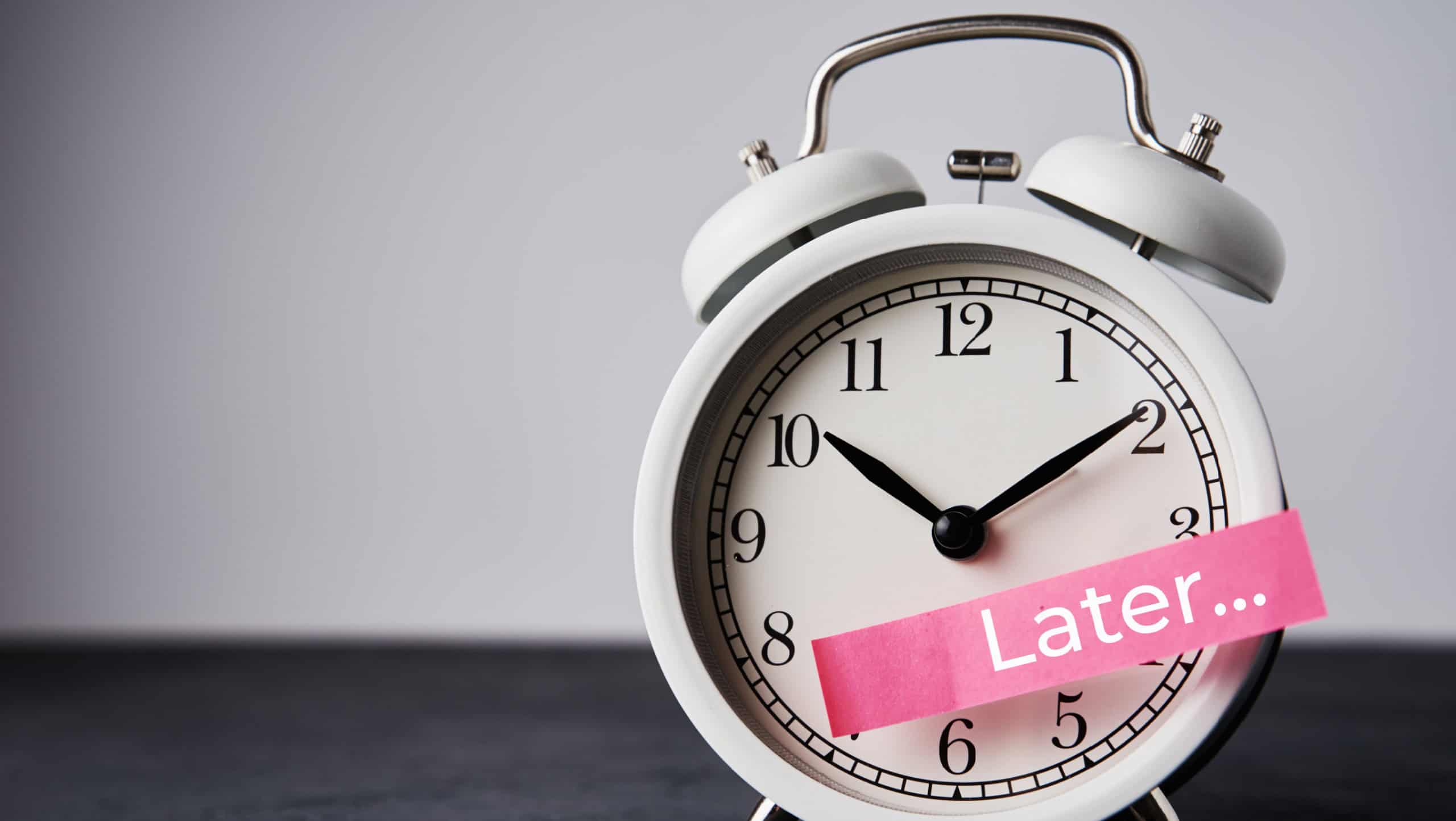 Procrastination and delay concept. Sticky note with word later on the white alarm clock. Urgency time