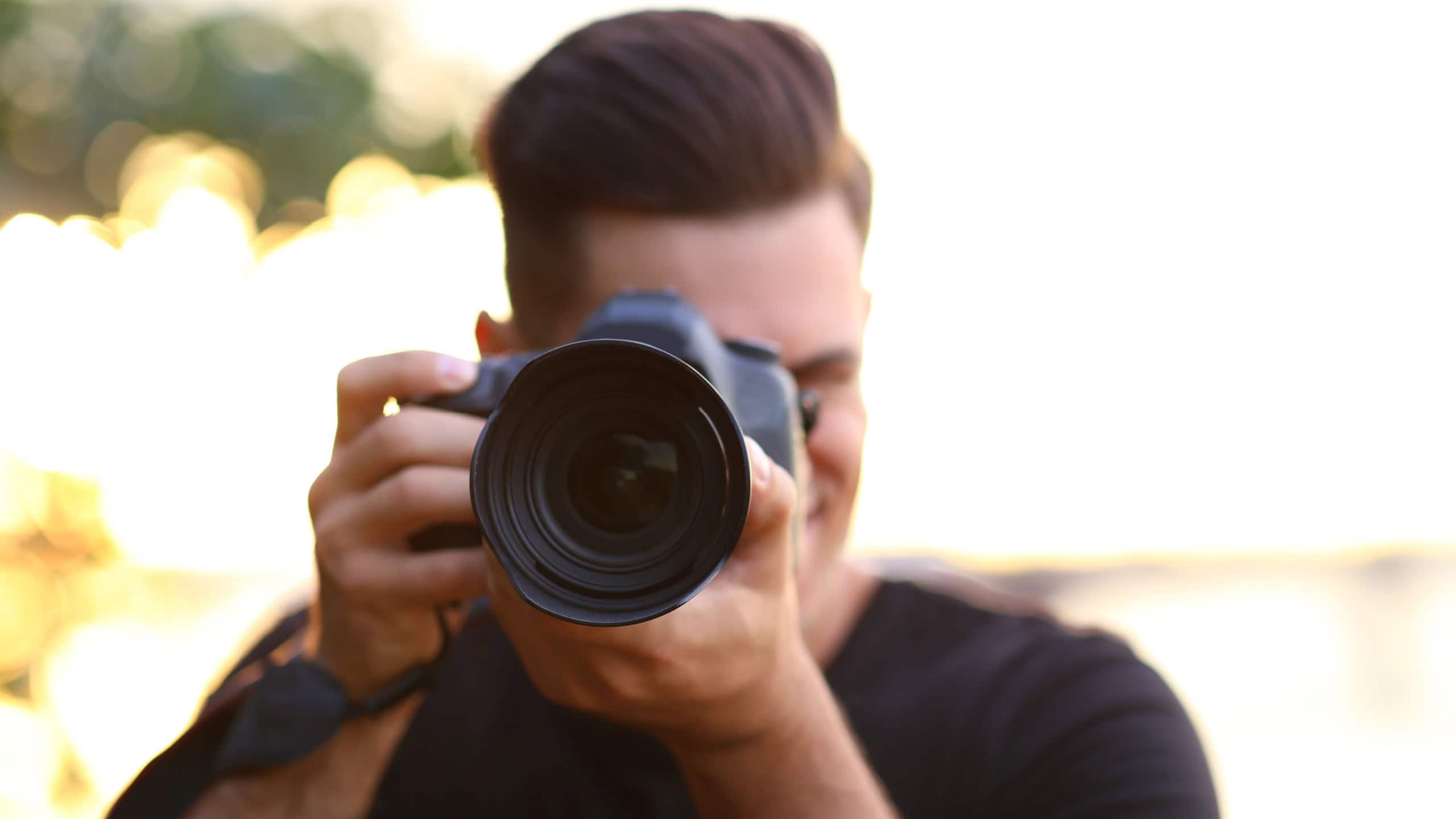 Photographer taking picture with professional camera in countryside, focus on lens
