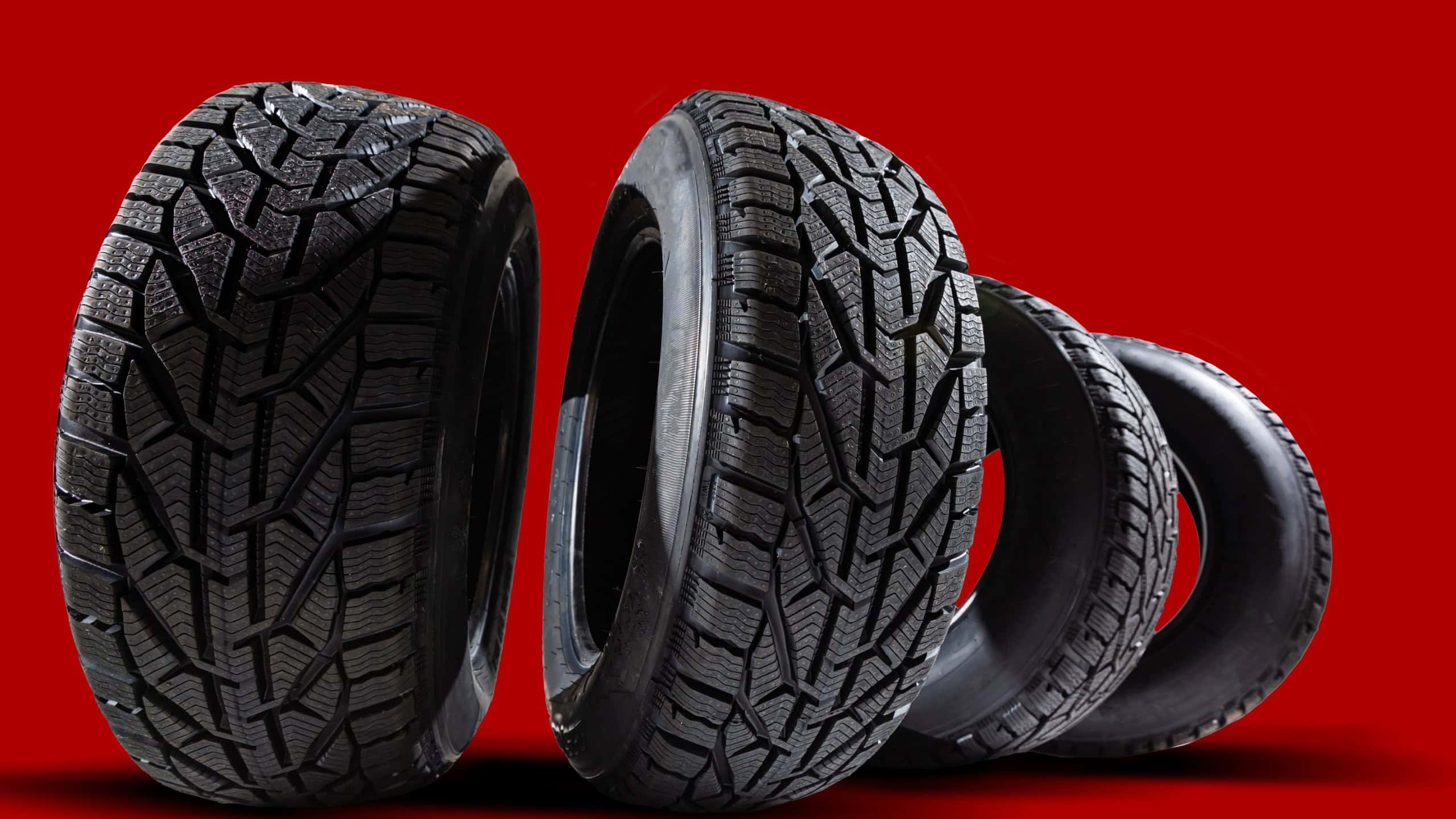 Stack of four new red tyres for winter car on blue background