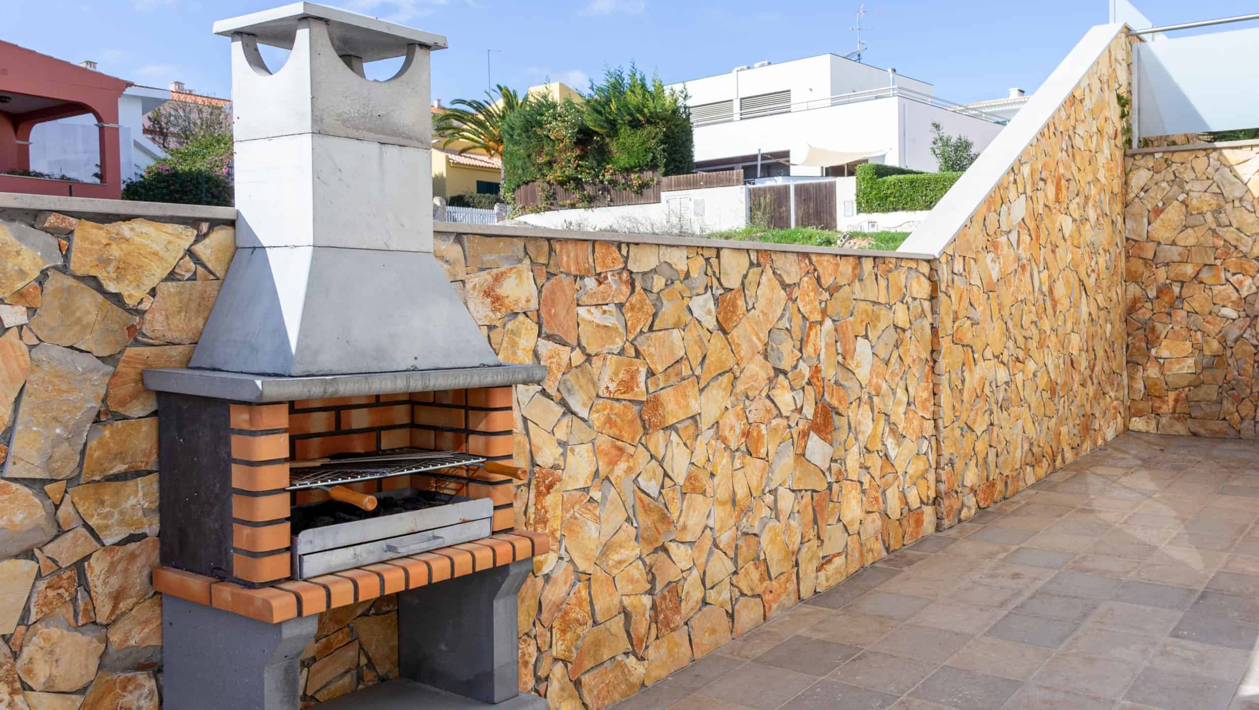 Simple and clean outdoors space with a barbecue to grill some meat. In the background there are some visible houses.