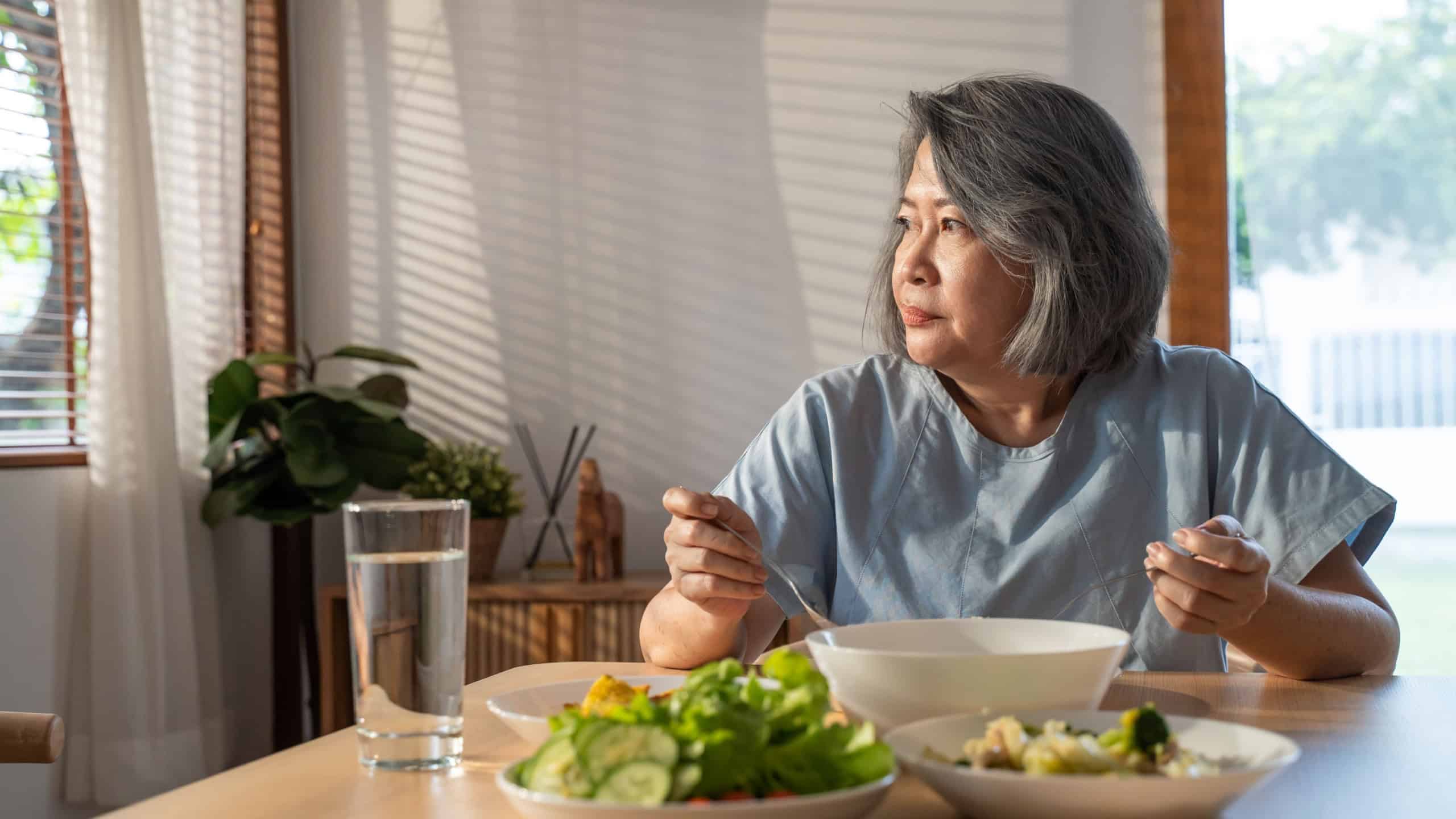 Asian Elderly retired grandmother stay at home with painful face sitting alone on eating table in house. Depressed mature Senior old woman upset feeling unhappy, lonely and missing his family at home