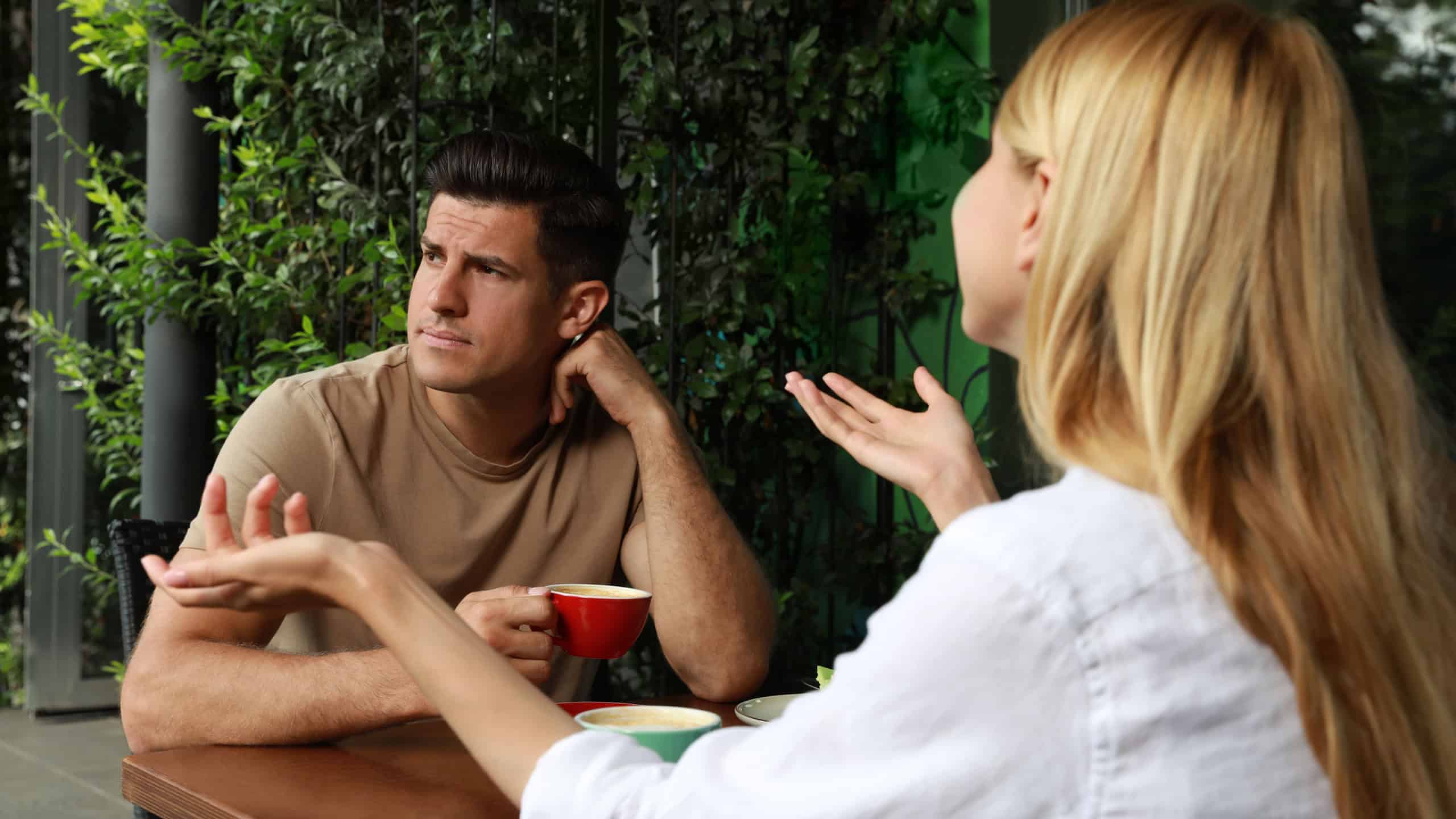 Man having boring date with talkative woman in outdoor cafe