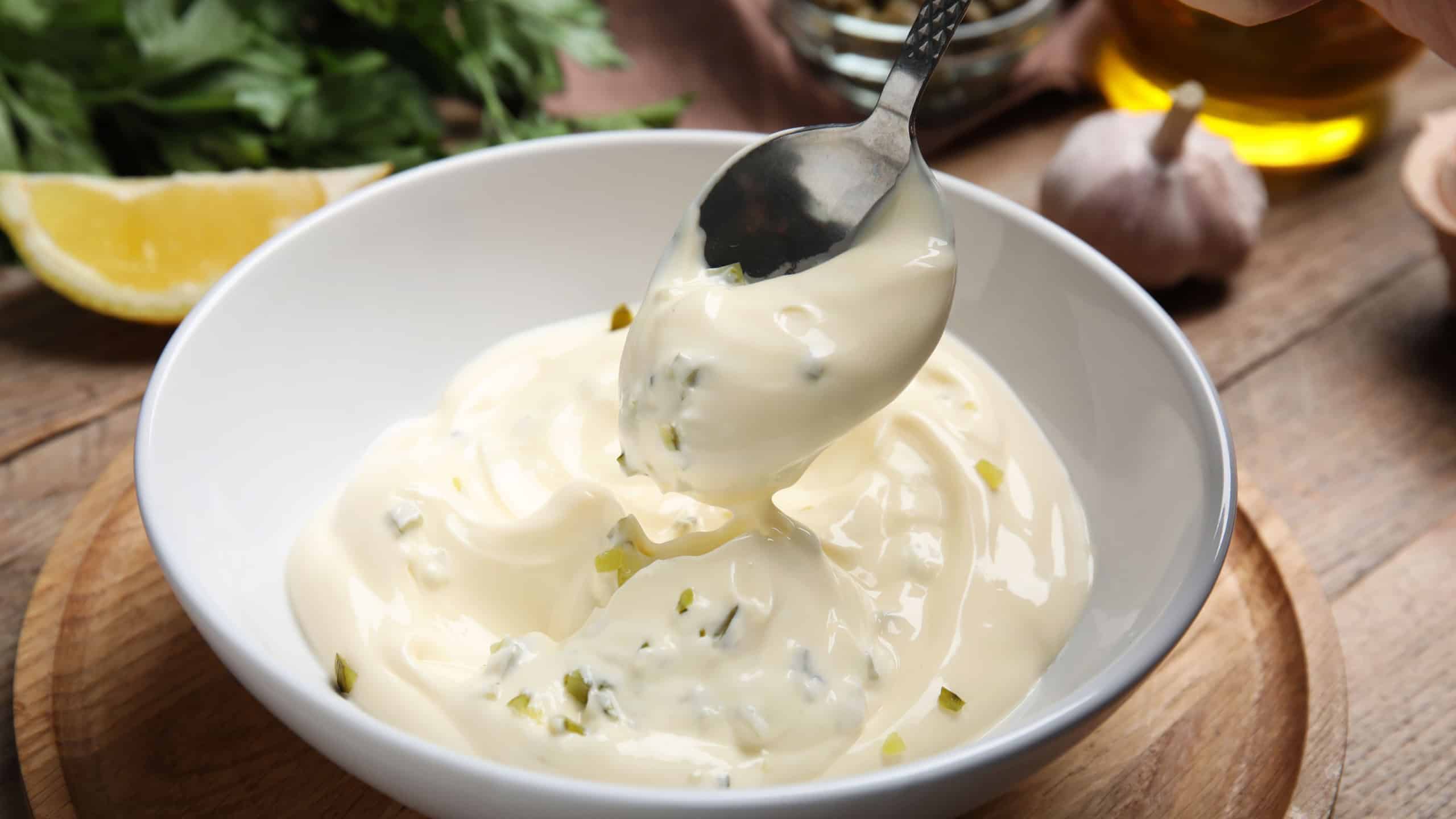 Delicious tartar sauce and spoon on wooden table, closeup
