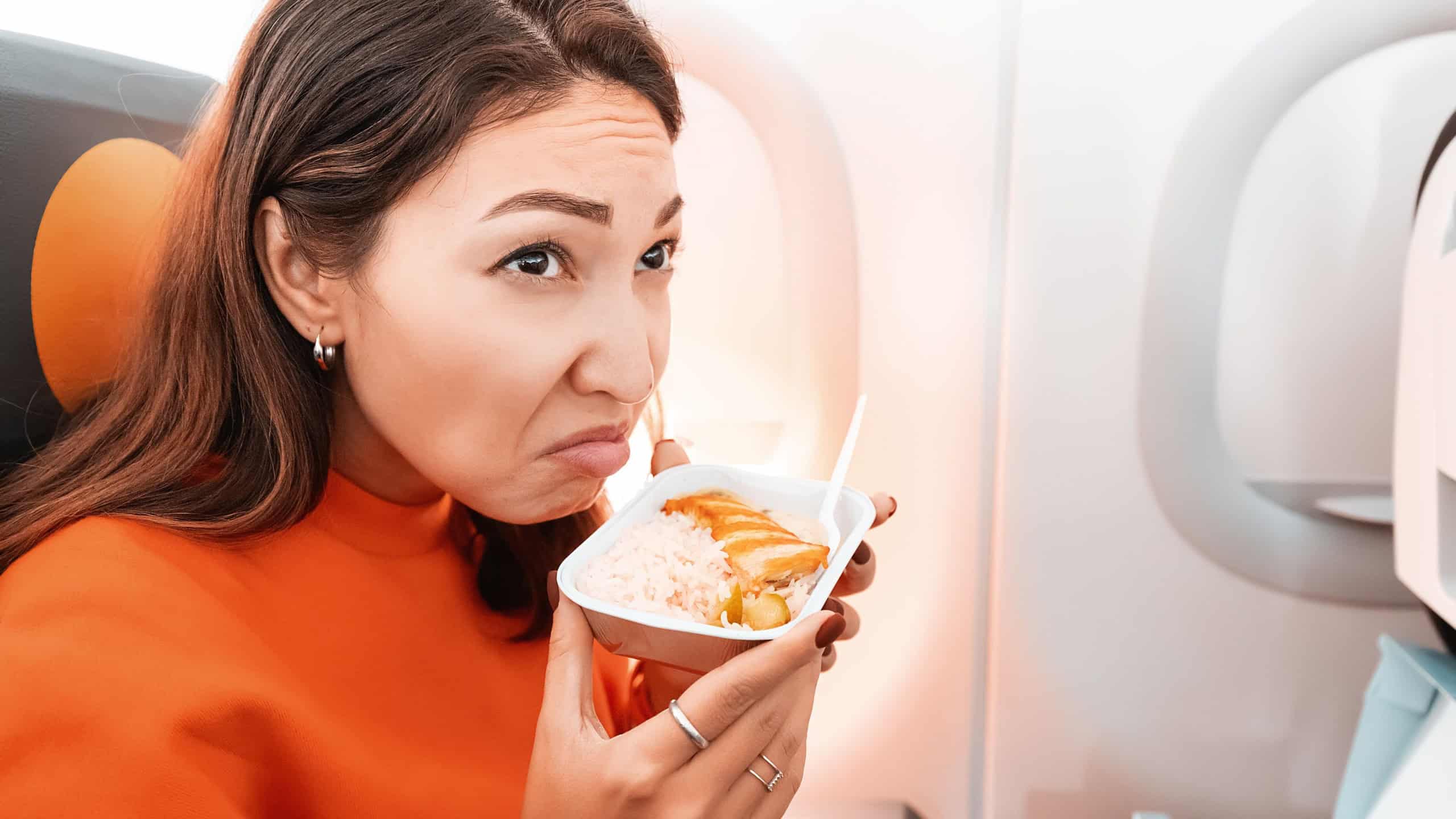 An annoyed woman sniffs a spoiled lunch on the plane. The concept of consumer protection