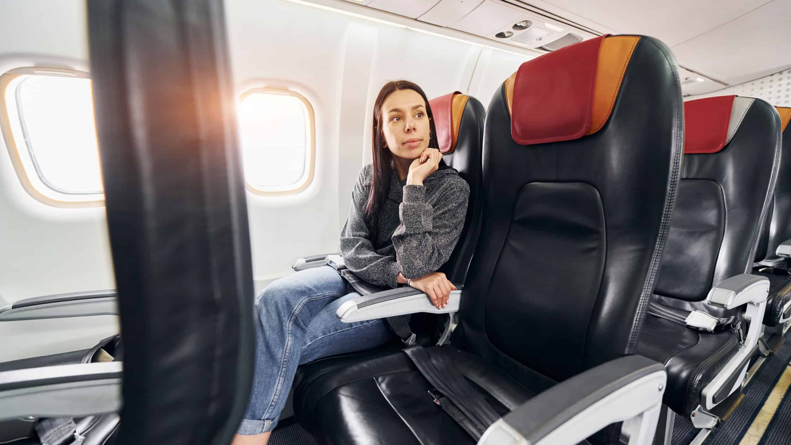 Young woman in casual clothes sits on the passenger seat in the plane.