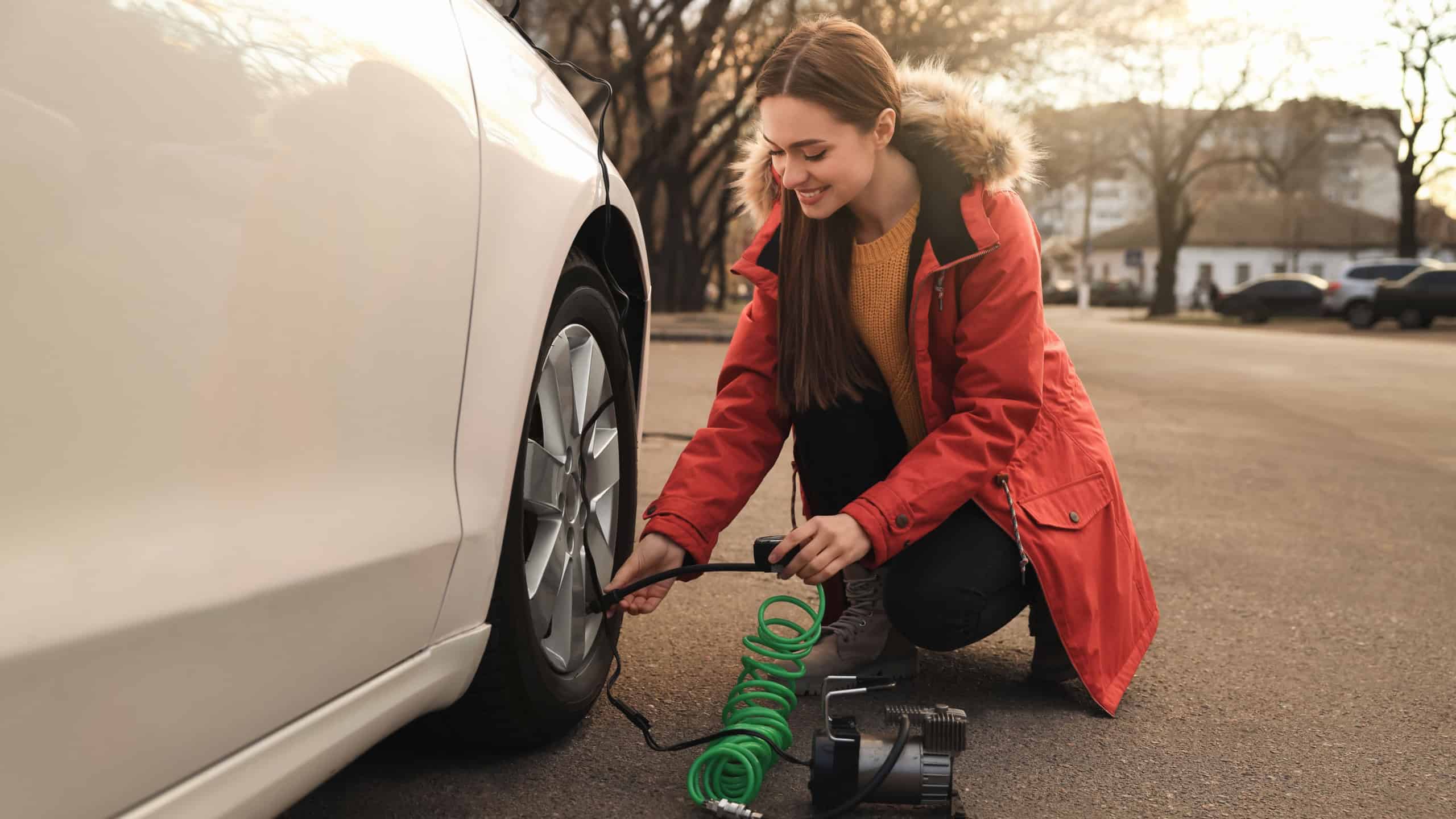 Young woman inflating car tire with air compressor on street