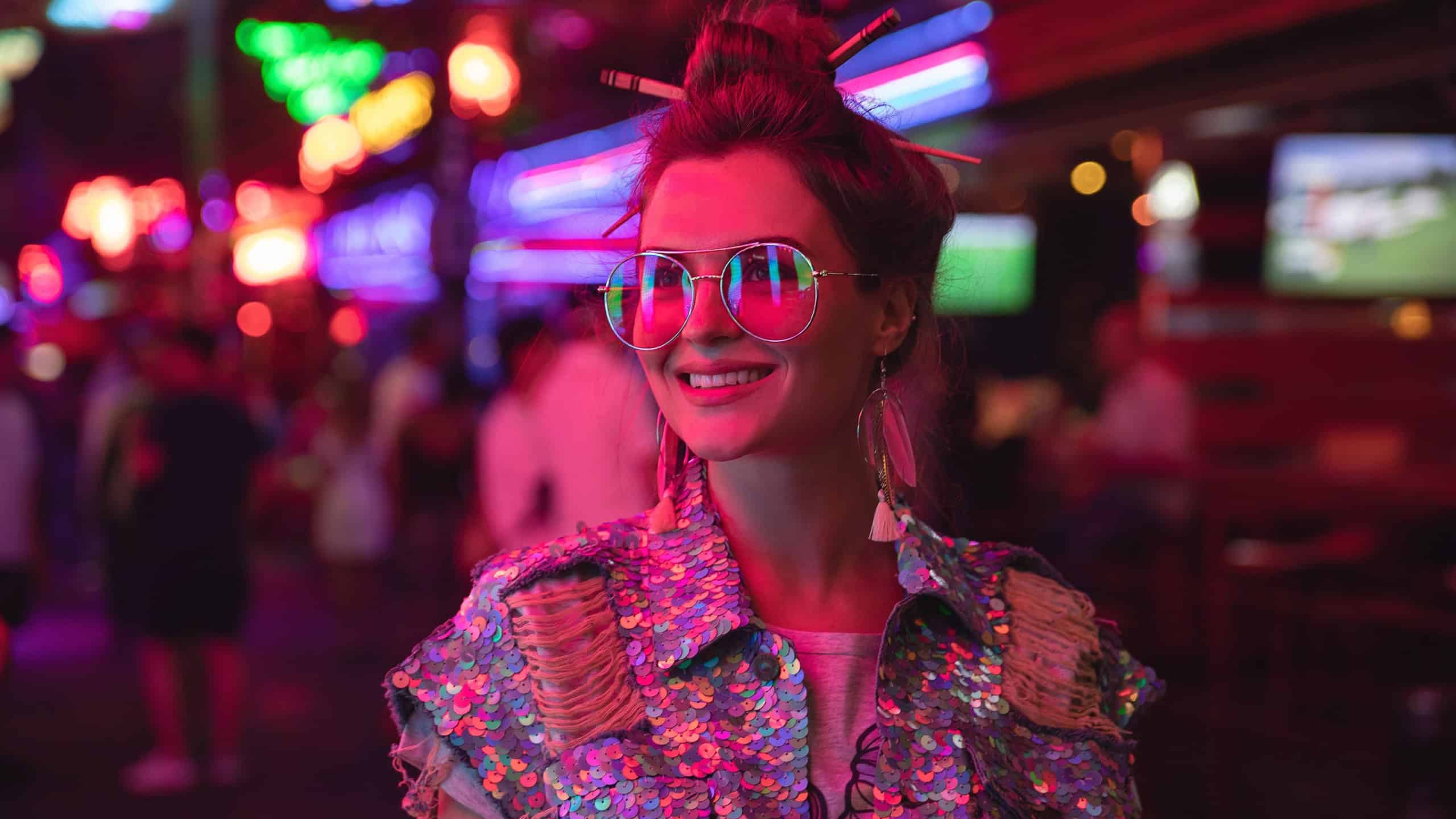 Young stylish woman wearing jacket with shining sequins on the city street with neon lights