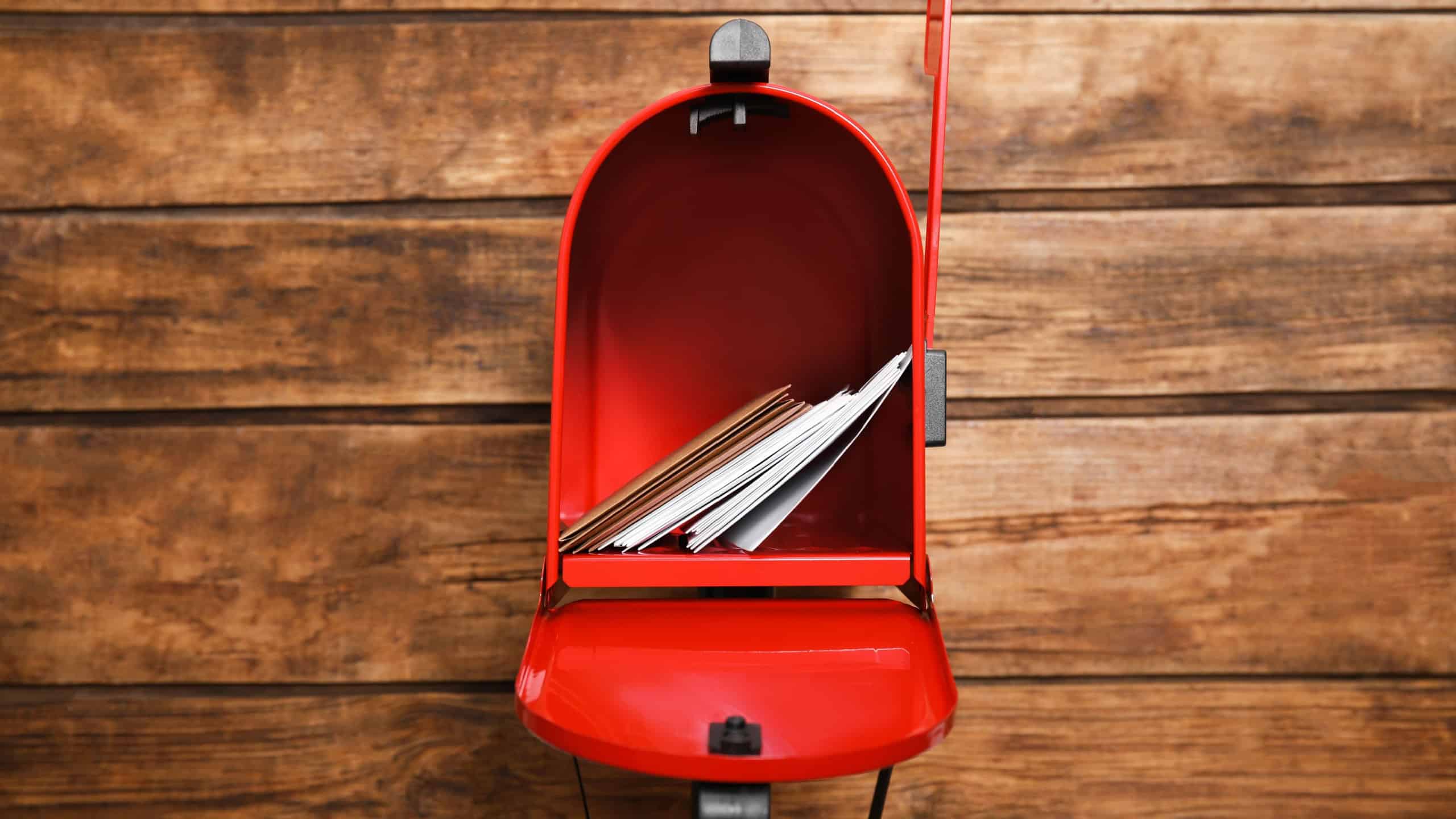 Open red letter box with envelopes against wooden background