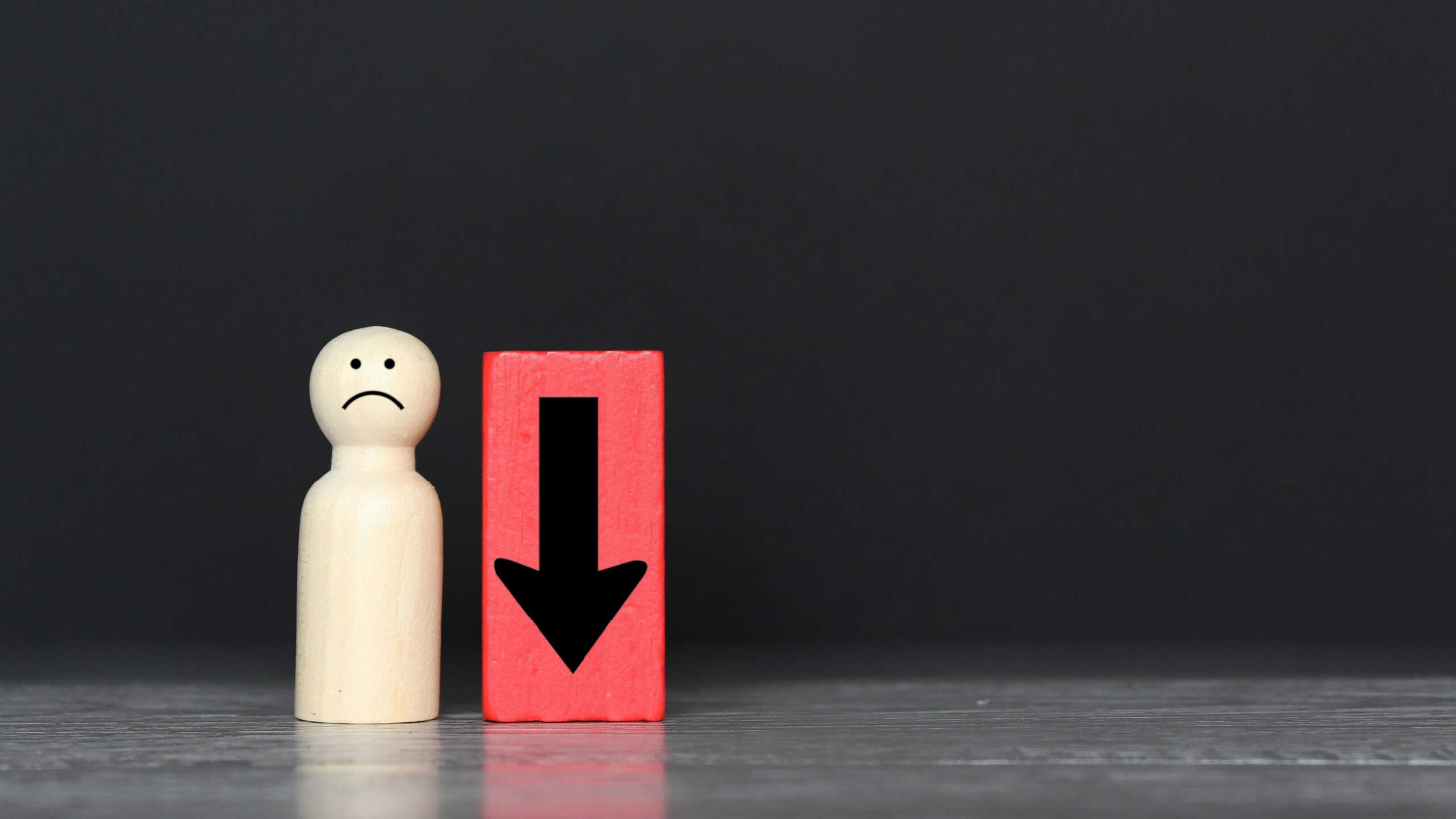 Wooden doll and downward arrow with copy space. Demote, low morale and feeling down concept