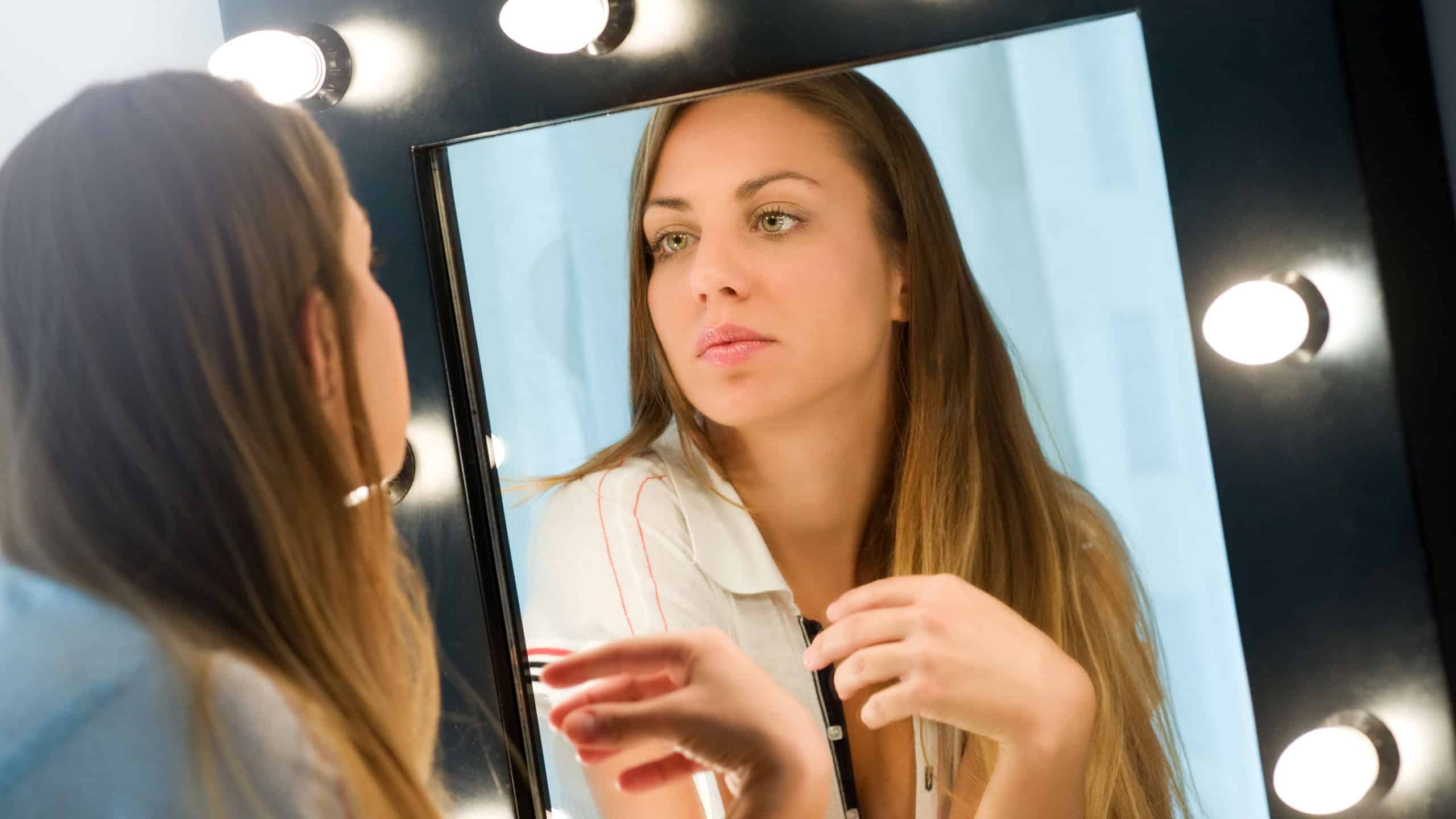 Young woman admiring herself in the mirror as she applies her makeup staring at her own reflection with a serious expression