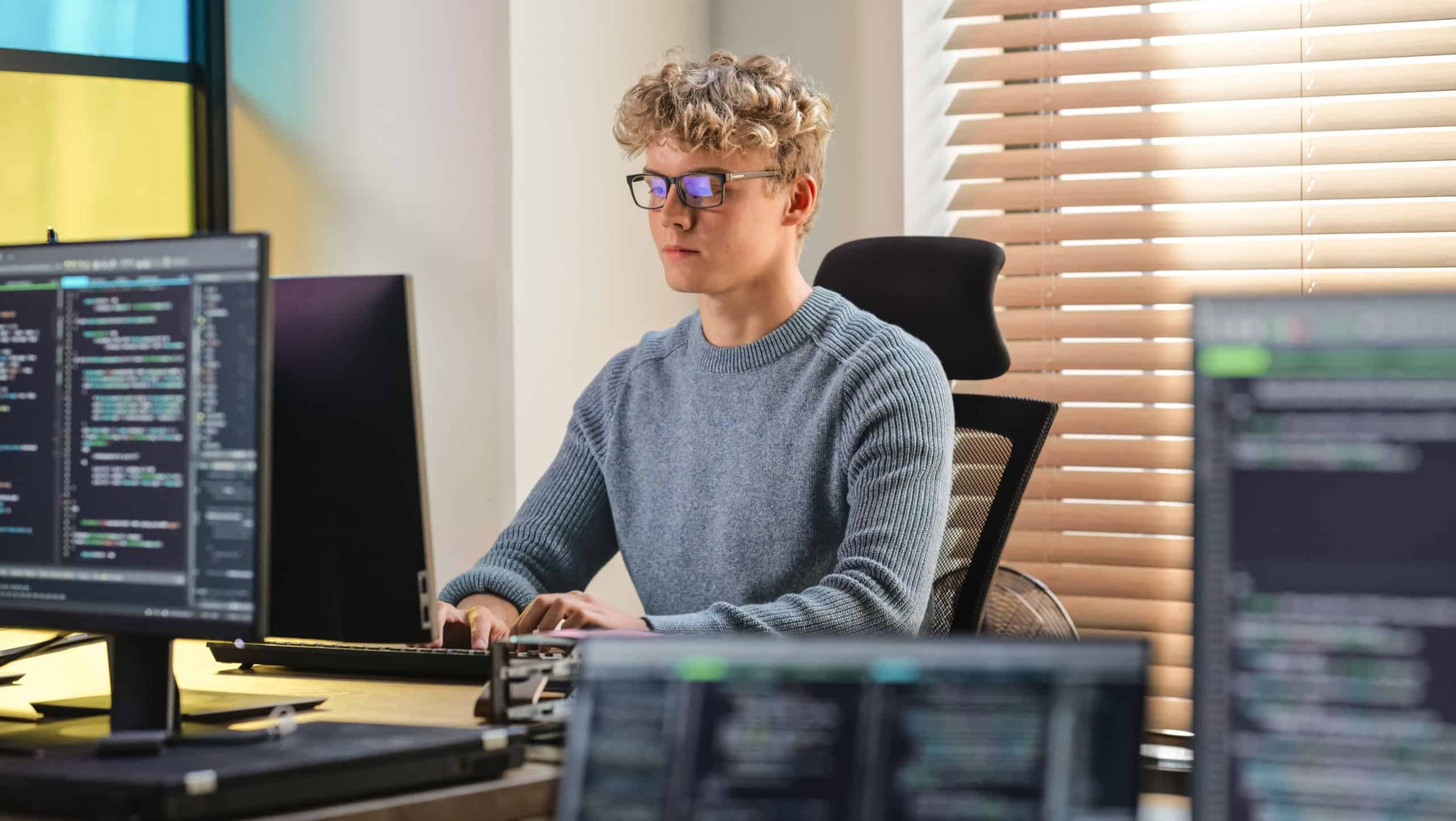 Male Software Engineer Coding On Desktop Computer in Creative Office Space. Young Caucasian Man Applying His Programming Skills in Innovative Technological Startup. Junior Developer Working.