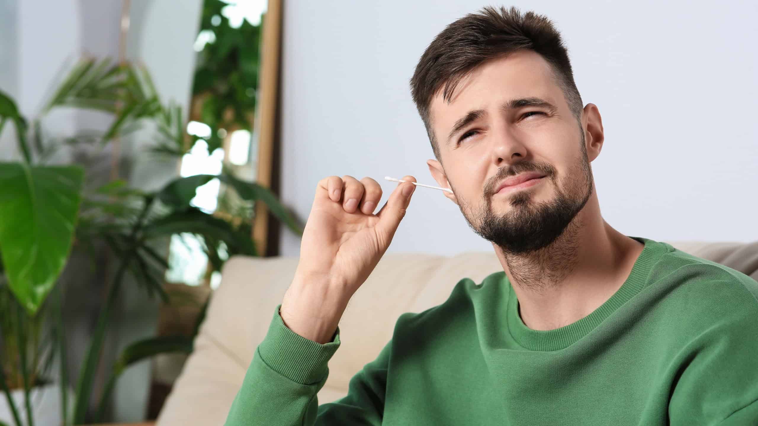 Young man cleaning ear with cotton swab at home. Space for text