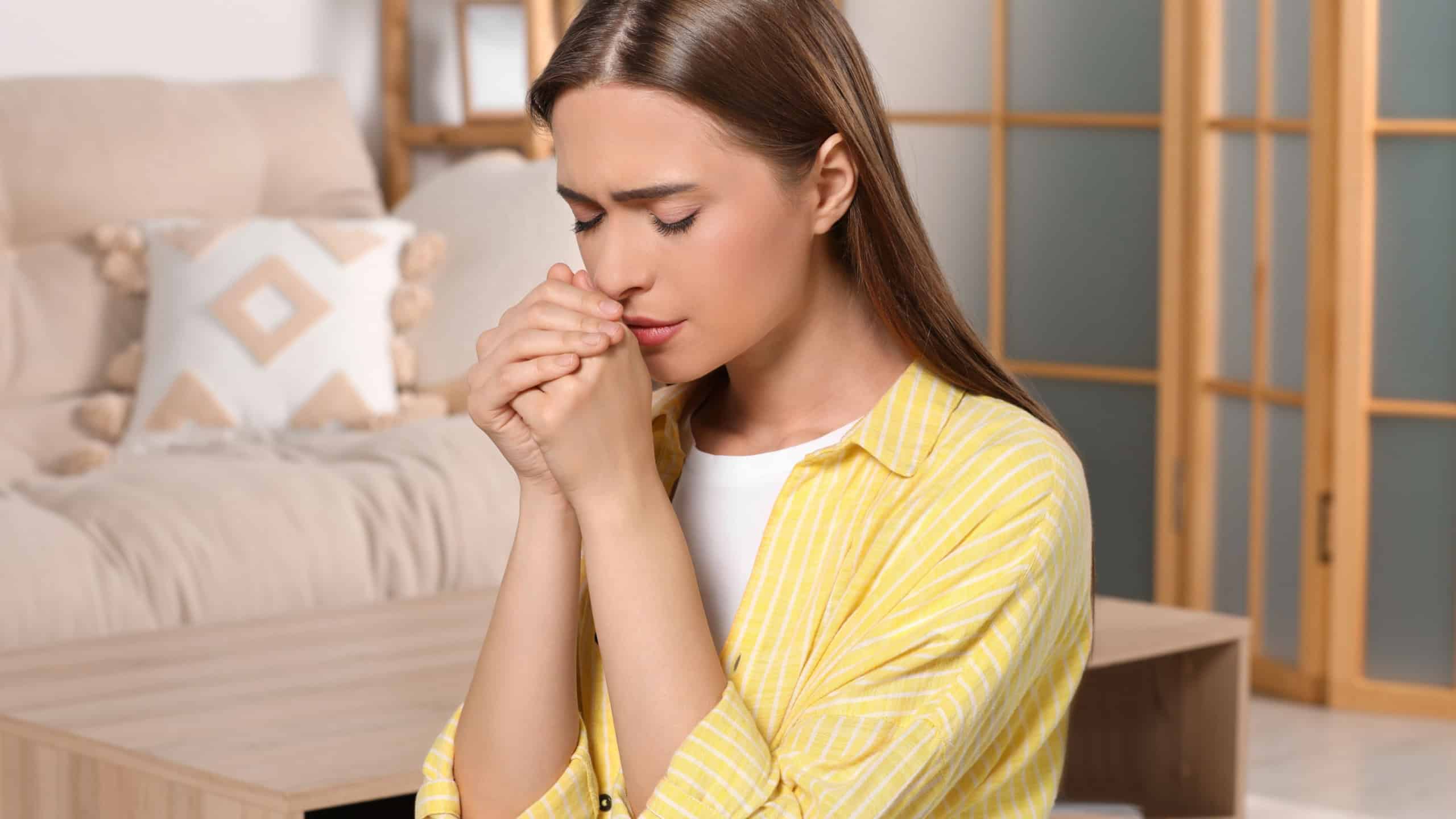 Woman with clasped hands praying at home