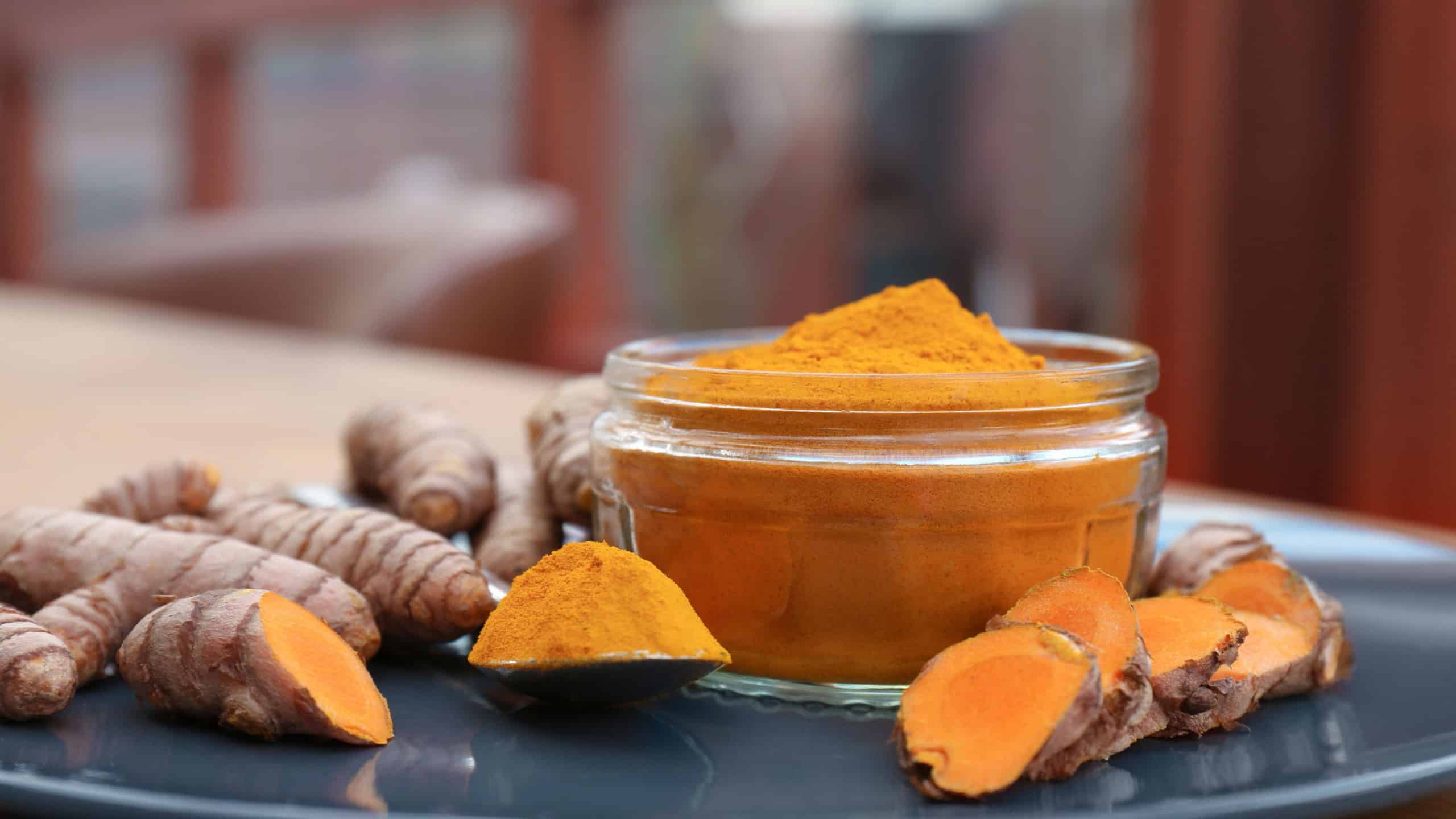 Plate with glass jar of turmeric powder and fresh roots on table