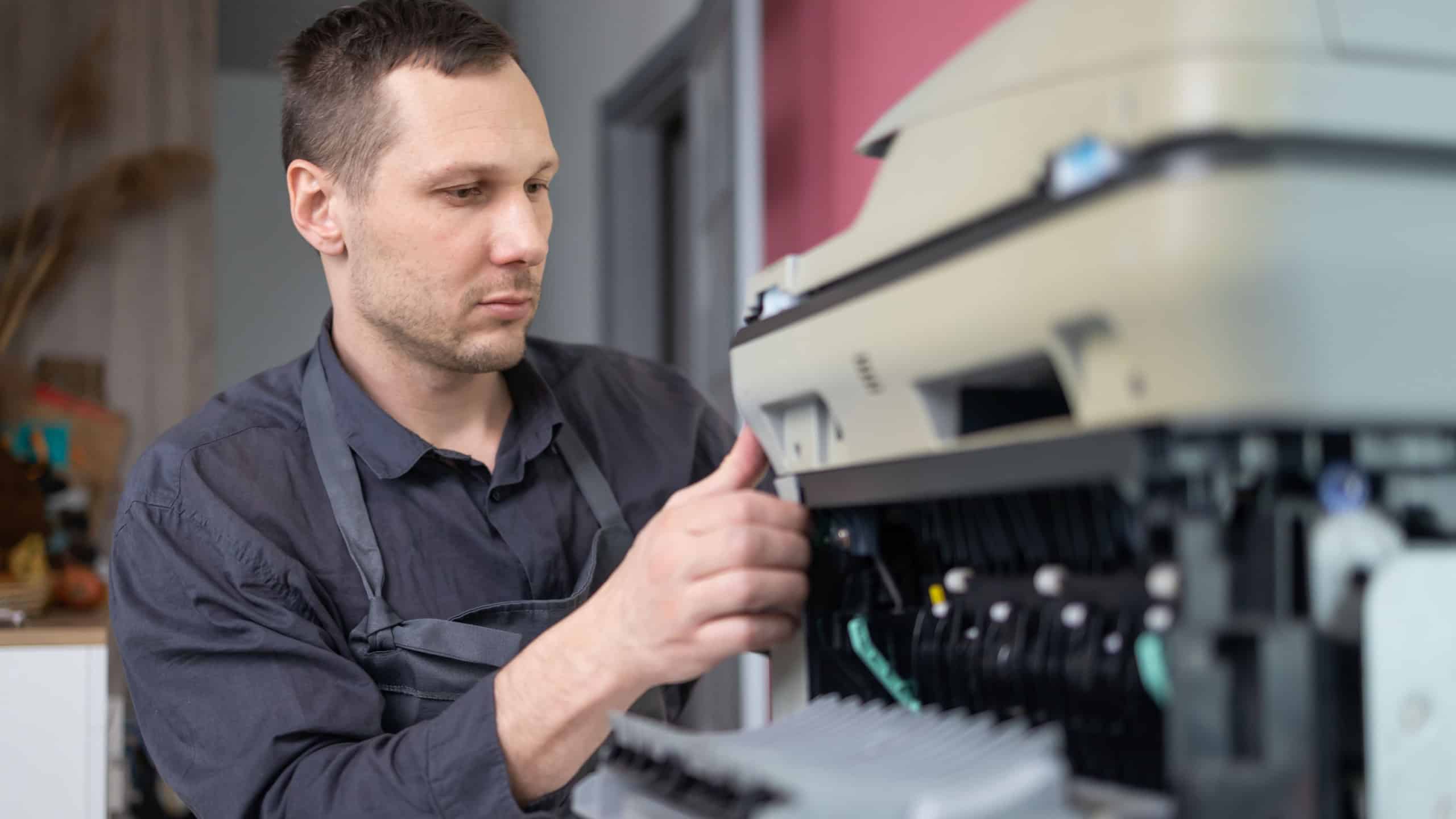 printer repair technician. A male handyman inspects a printer before starting repairs in a client's apartment.