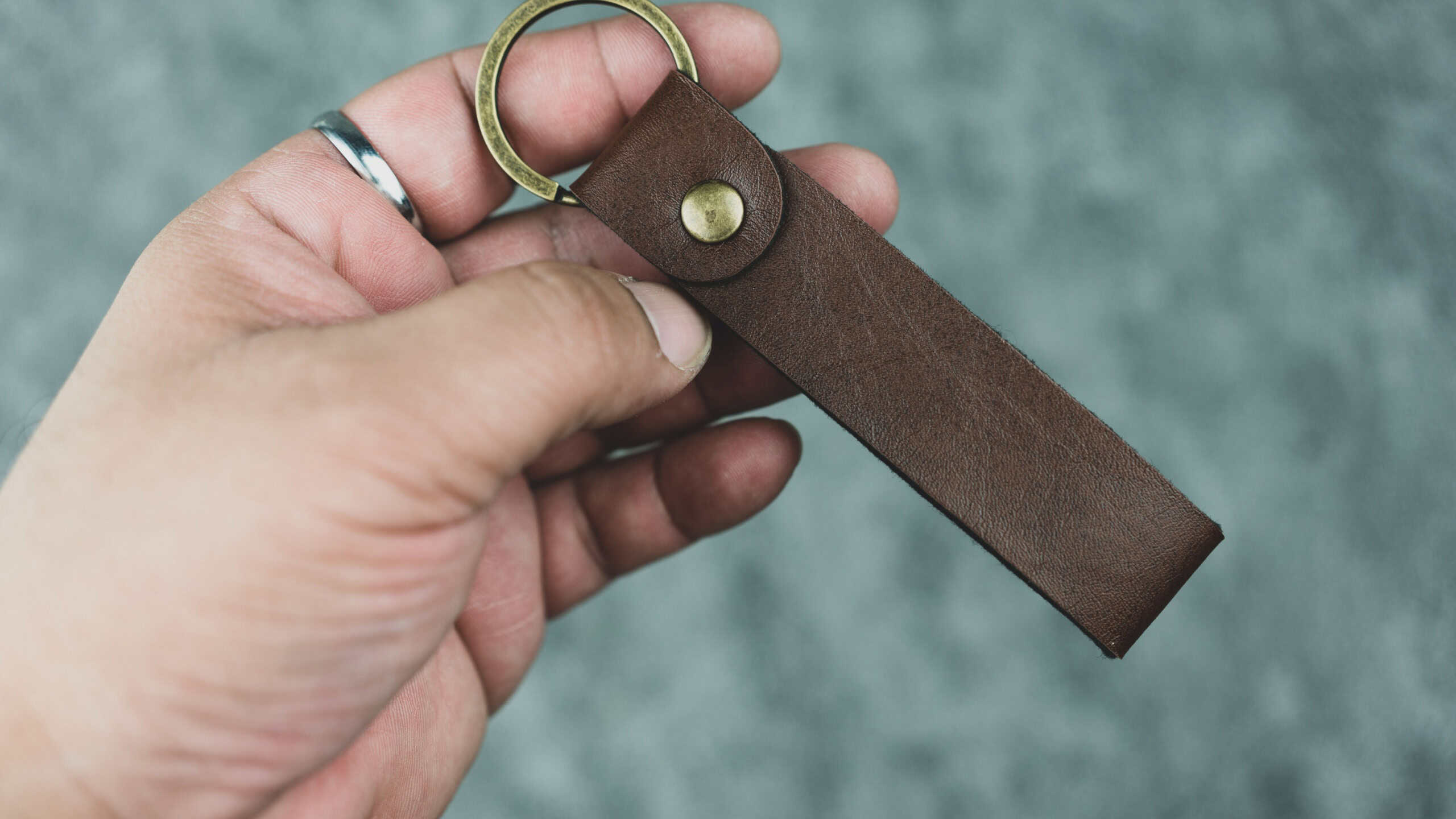 Hand holding empty of a brown keychain in imitation leather ready for you put mark and logo. Close up
