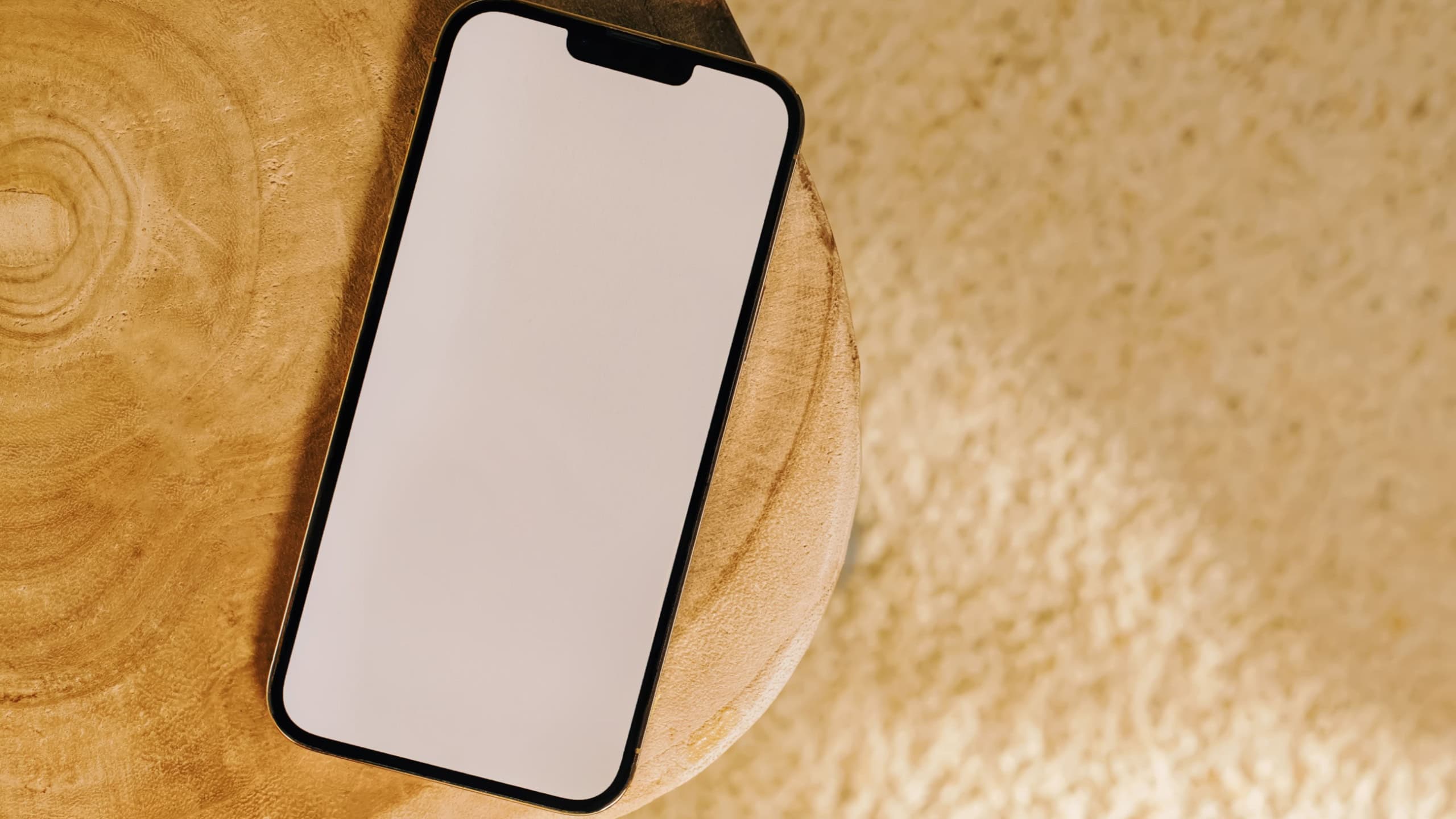 Smart phone mock-up in natural light, phone with white screen on small wooden side table, view from the top