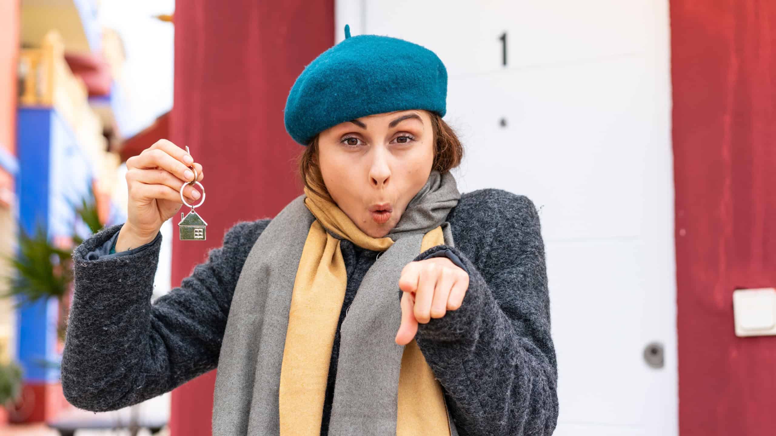 Brunette woman holding home keys at outdoors surprised and pointing front