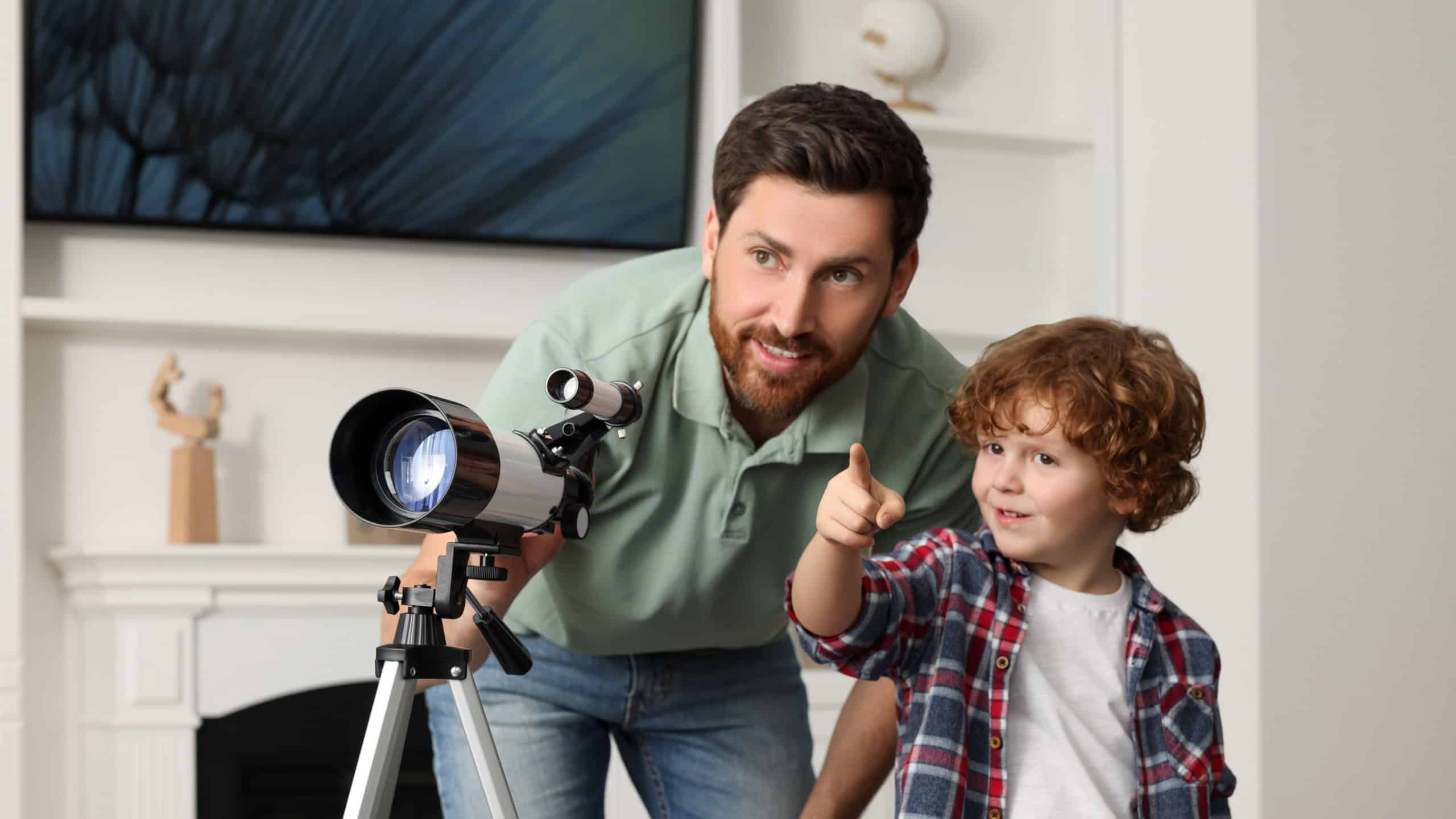 Father and son enjoying stargazing with a telescope in a cozy living room.