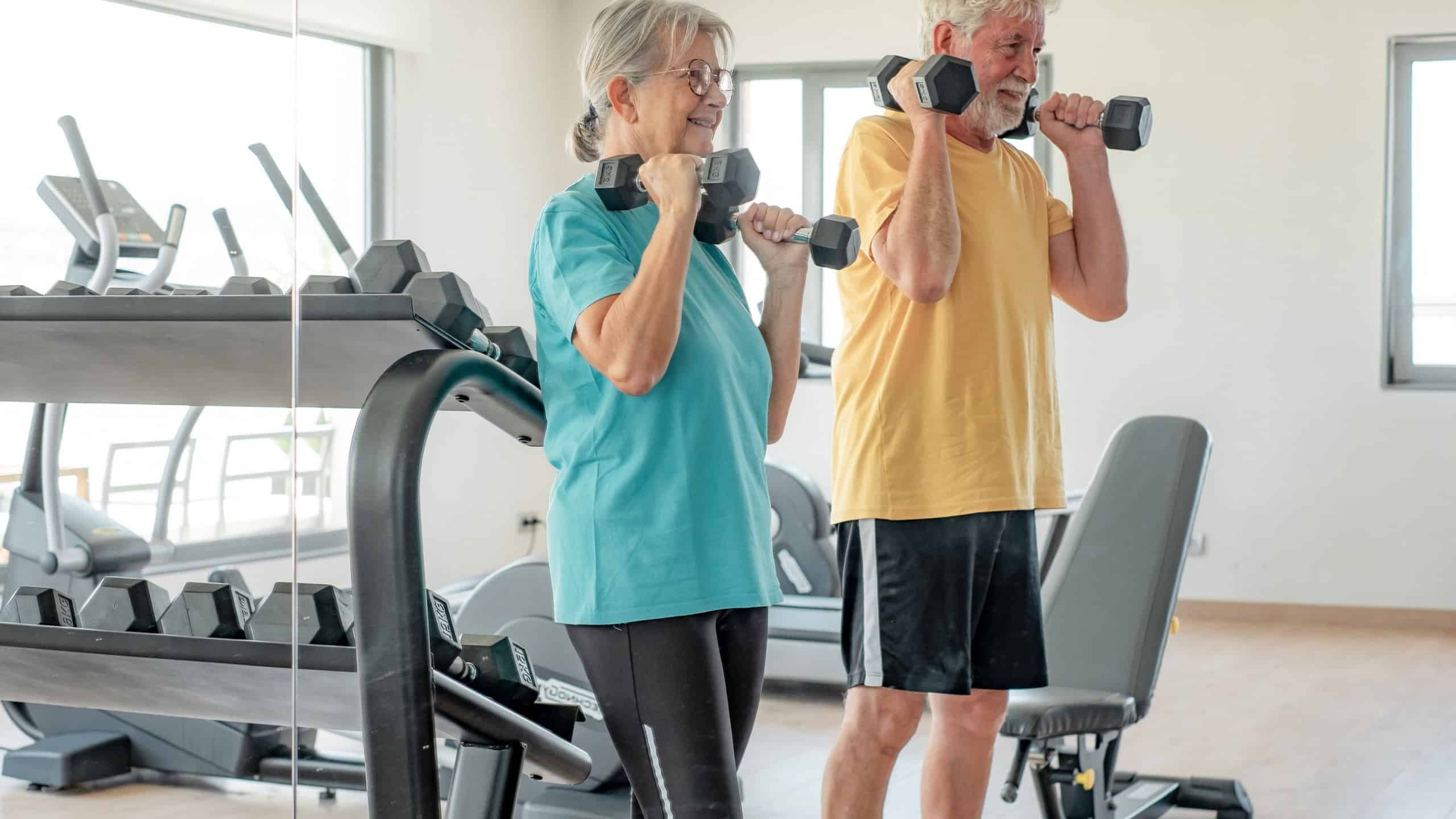 Athletic senior couple keeping fit working out together in the gym doing dumbbell lifting exercise. Sports life as a retiree