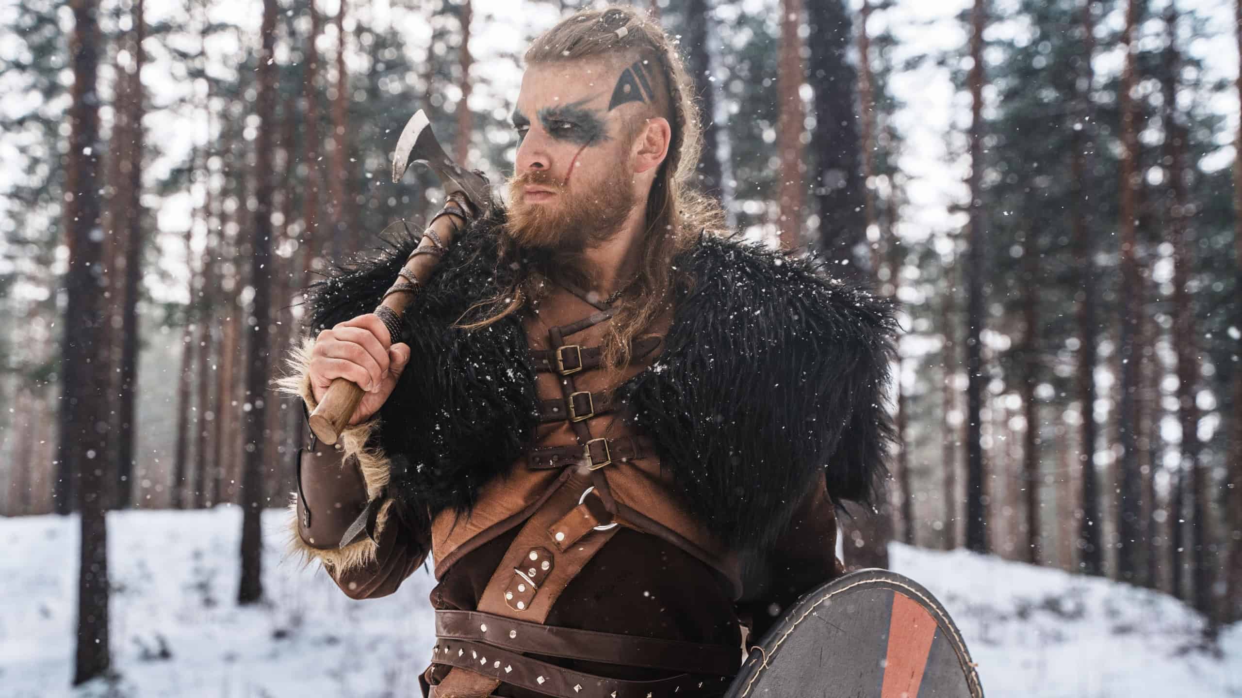 A fierce Viking warrior poised with an axe and shield in a snowy pine forest, depicting strength and historical Nordic culture