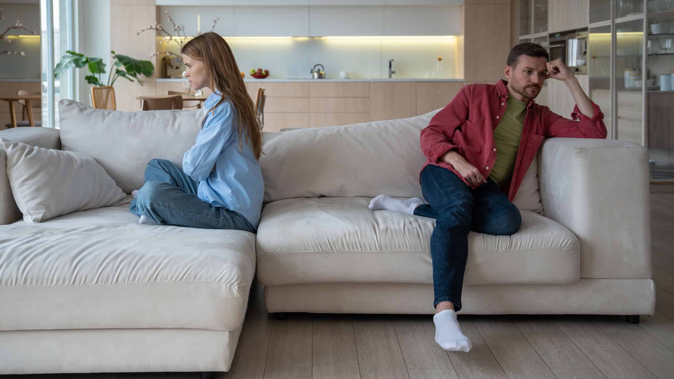 Unhappy couple having family problems sits on sofa at home, avoiding difficult conversation.