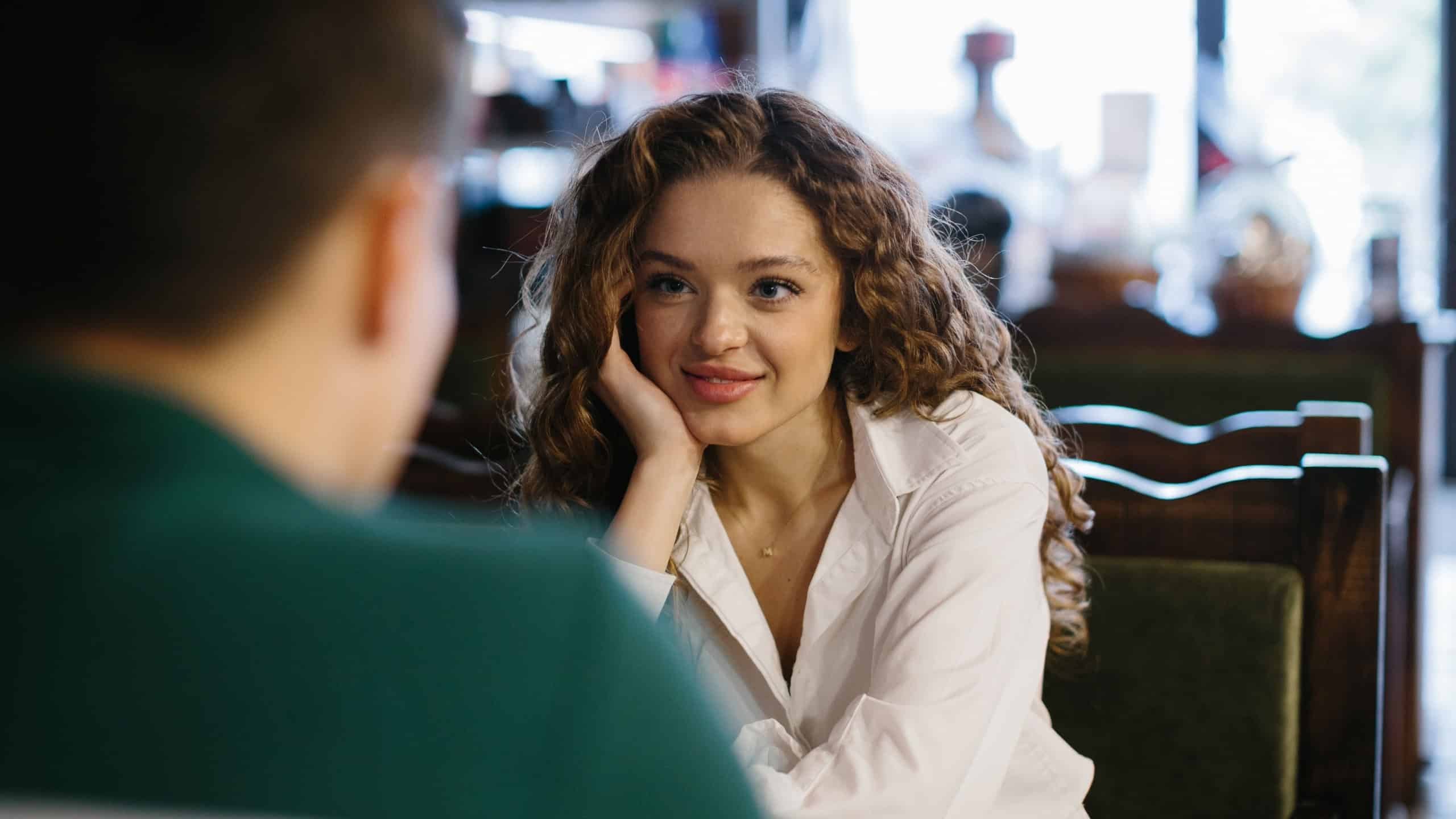 Smiling young woman talking to male friend boyfriend at meeting or romantic date in cafe