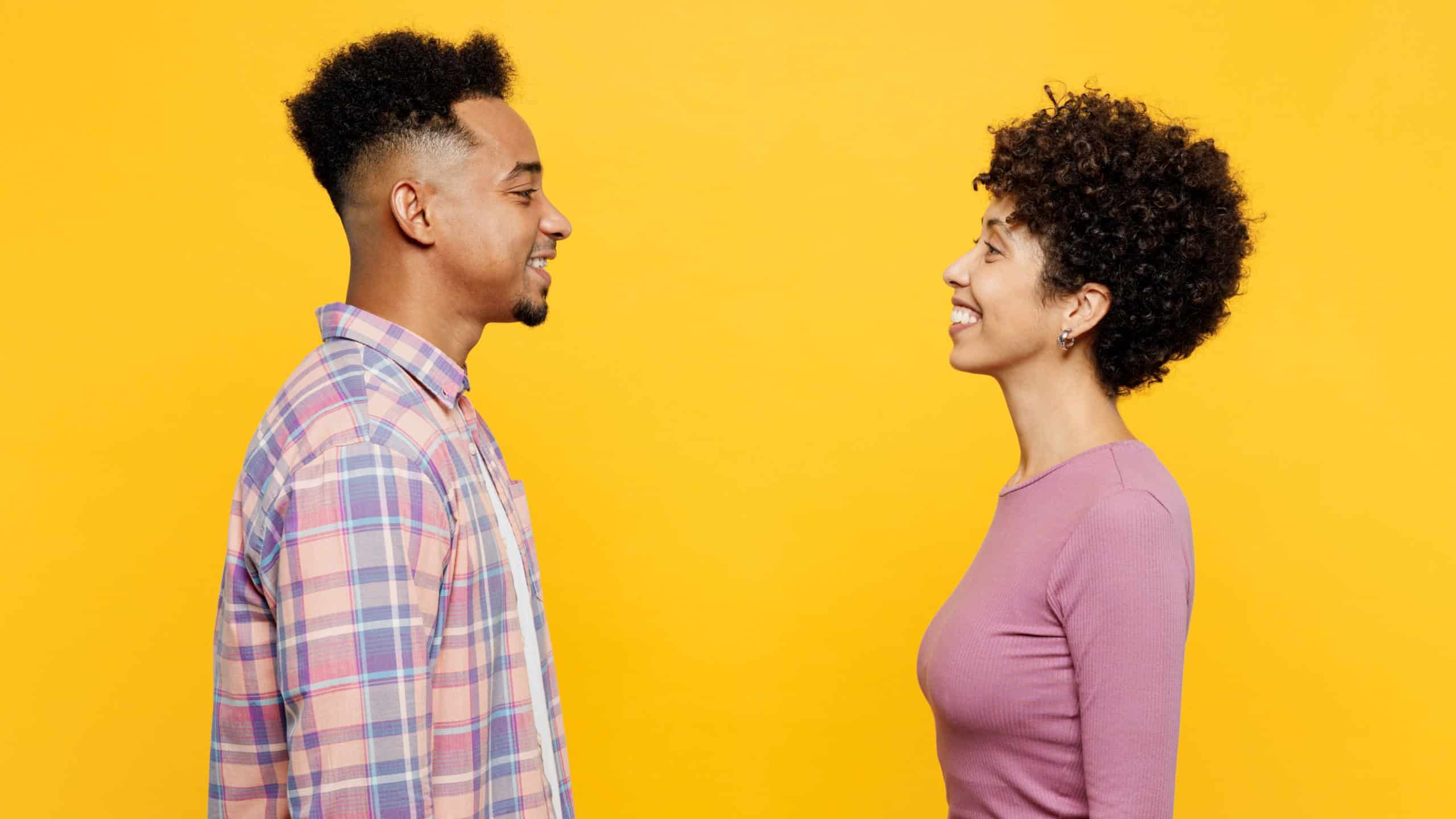 Side profile view young happy couple two friends family man woman of African American ethnicity wear purple casual clothes together look to each other isolated on plain yellow orange background studio