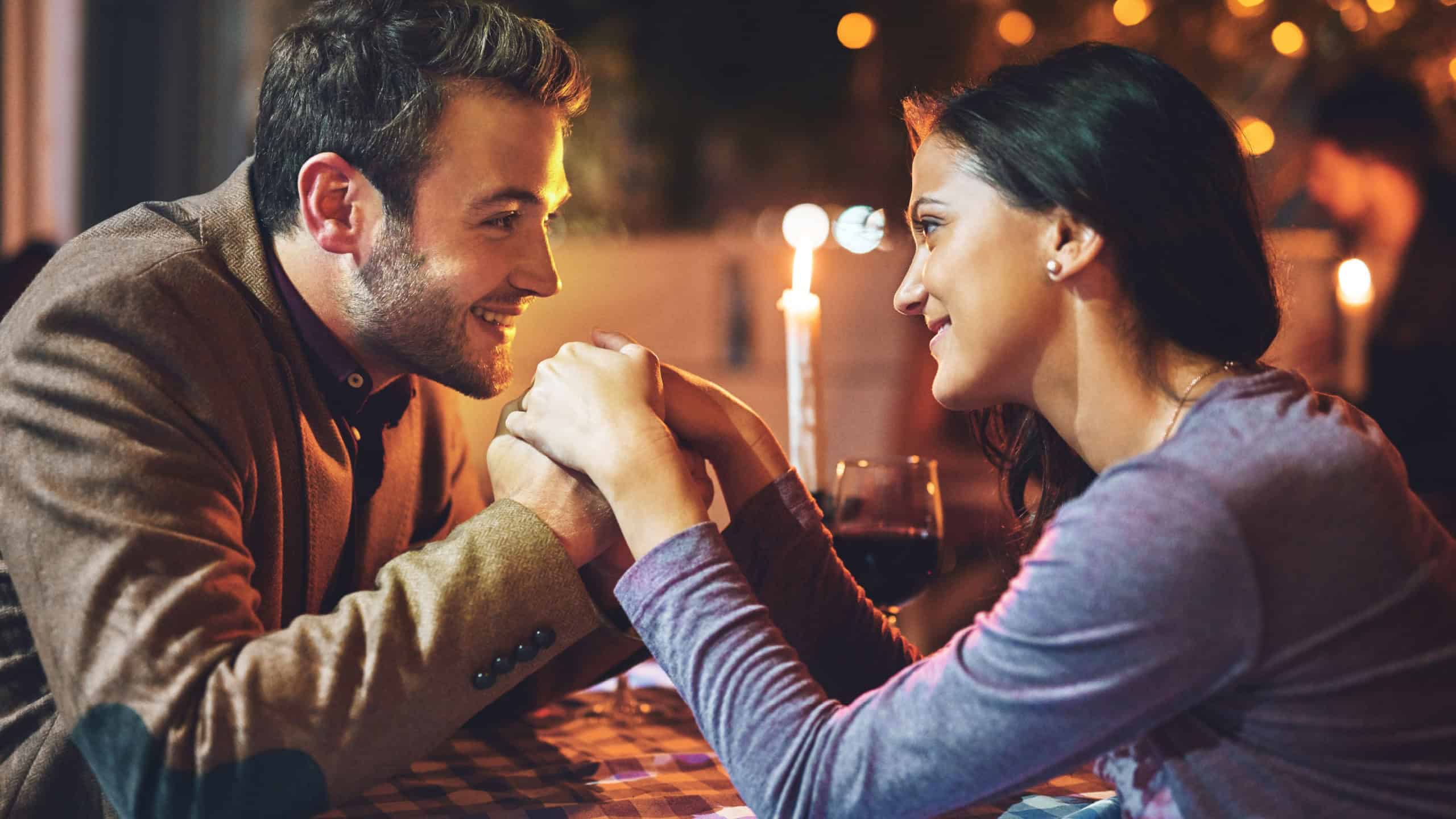 Couple, night and date holding hands for romance, love and anniversary at restaurant with candles. Man, woman and smile for fine dining, celebration and happiness together for valentines diner