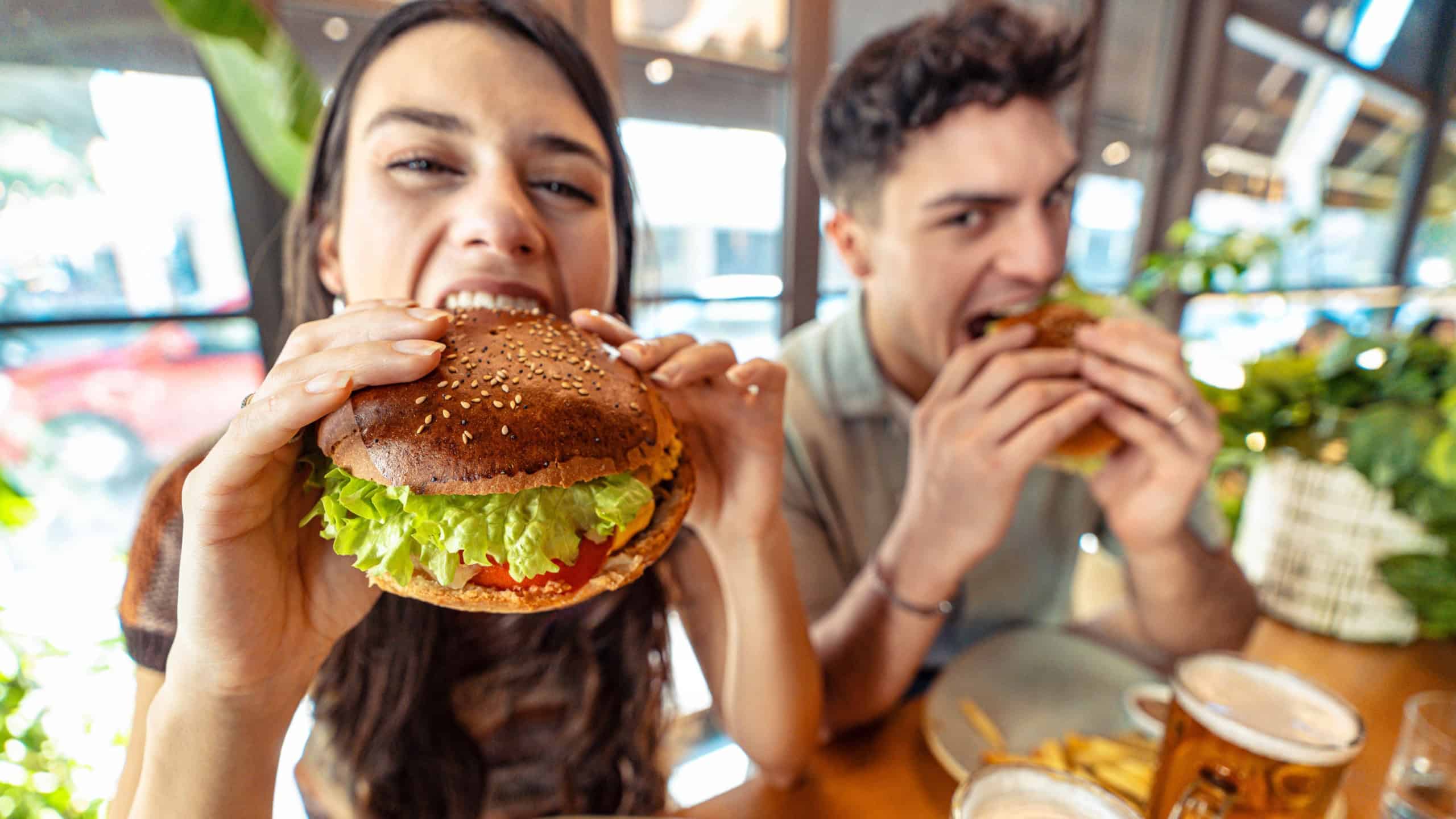 Couple eating fresh burger sitting at pub restaurant table