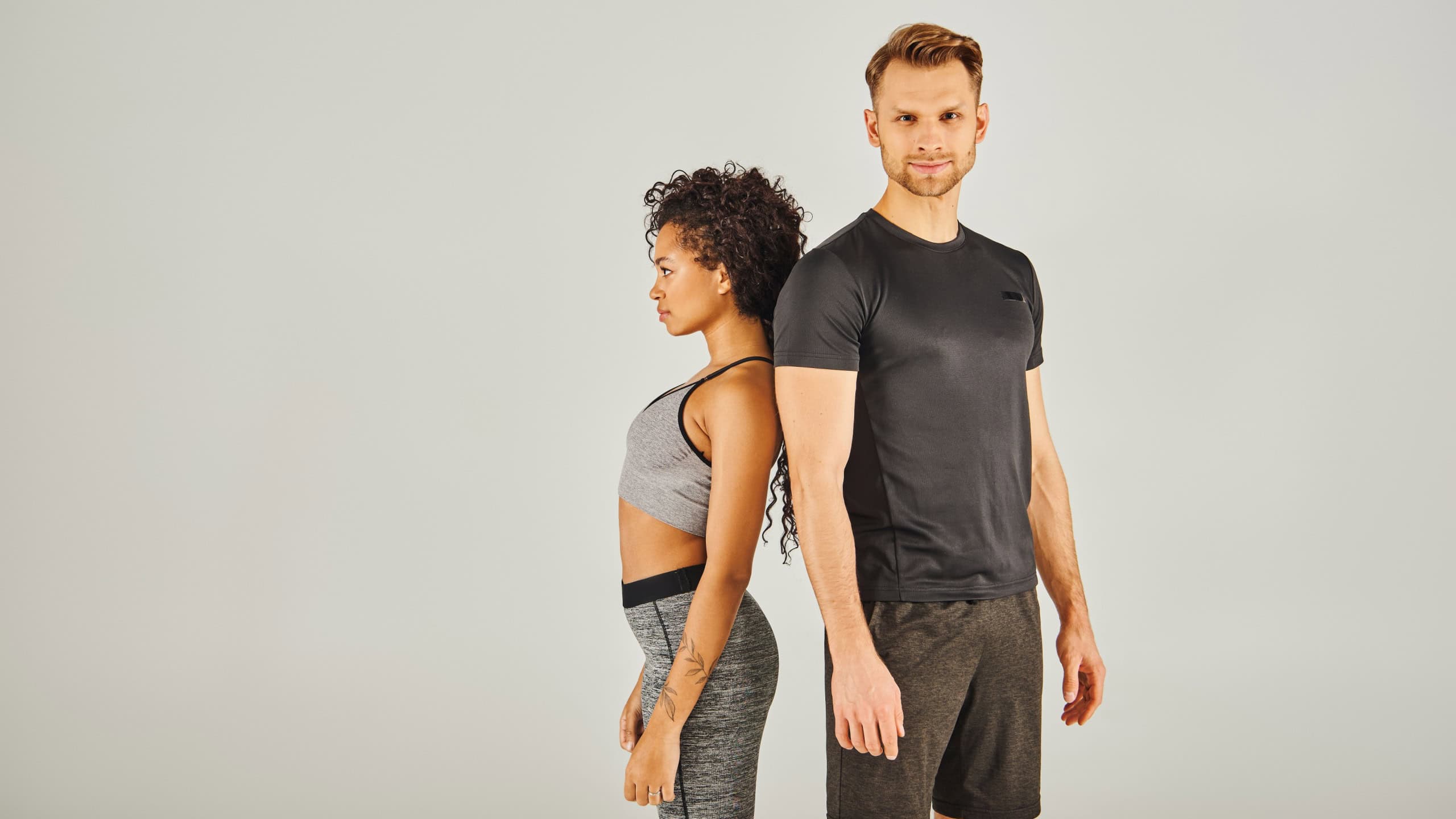 Young interracial sport couple confidently stands in front of a gray background, exuding strength and unity.