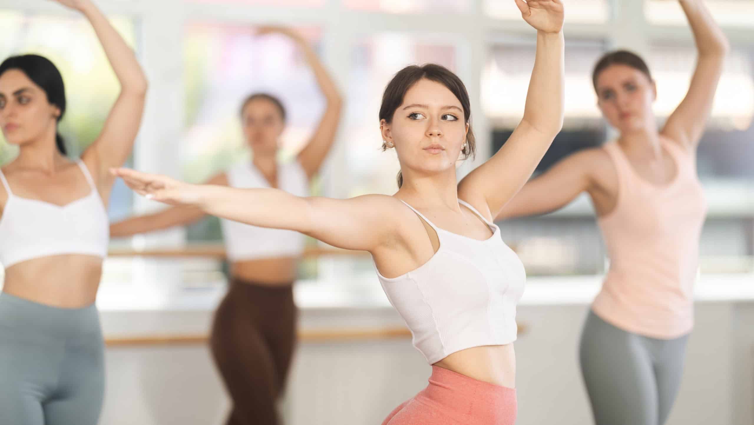 Big plan of gracile young woman doing choreography together with other participants of ballet classes
