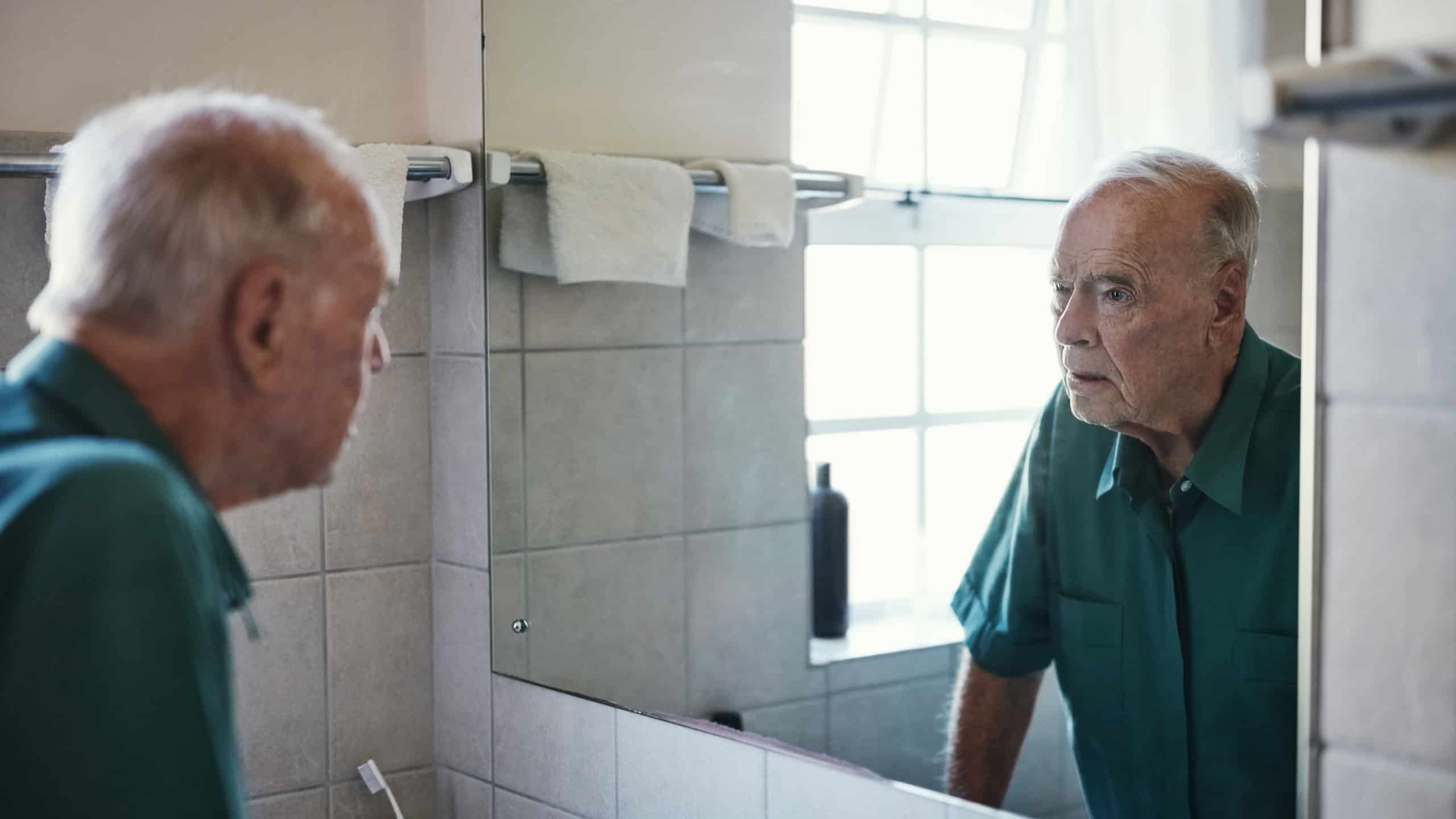 Reflection, elderly man and thinking in bathroom for retirement, healthcare and wellness. Remember, mirror and male person with Alzheimers, mental health and home for memory problem in apartment