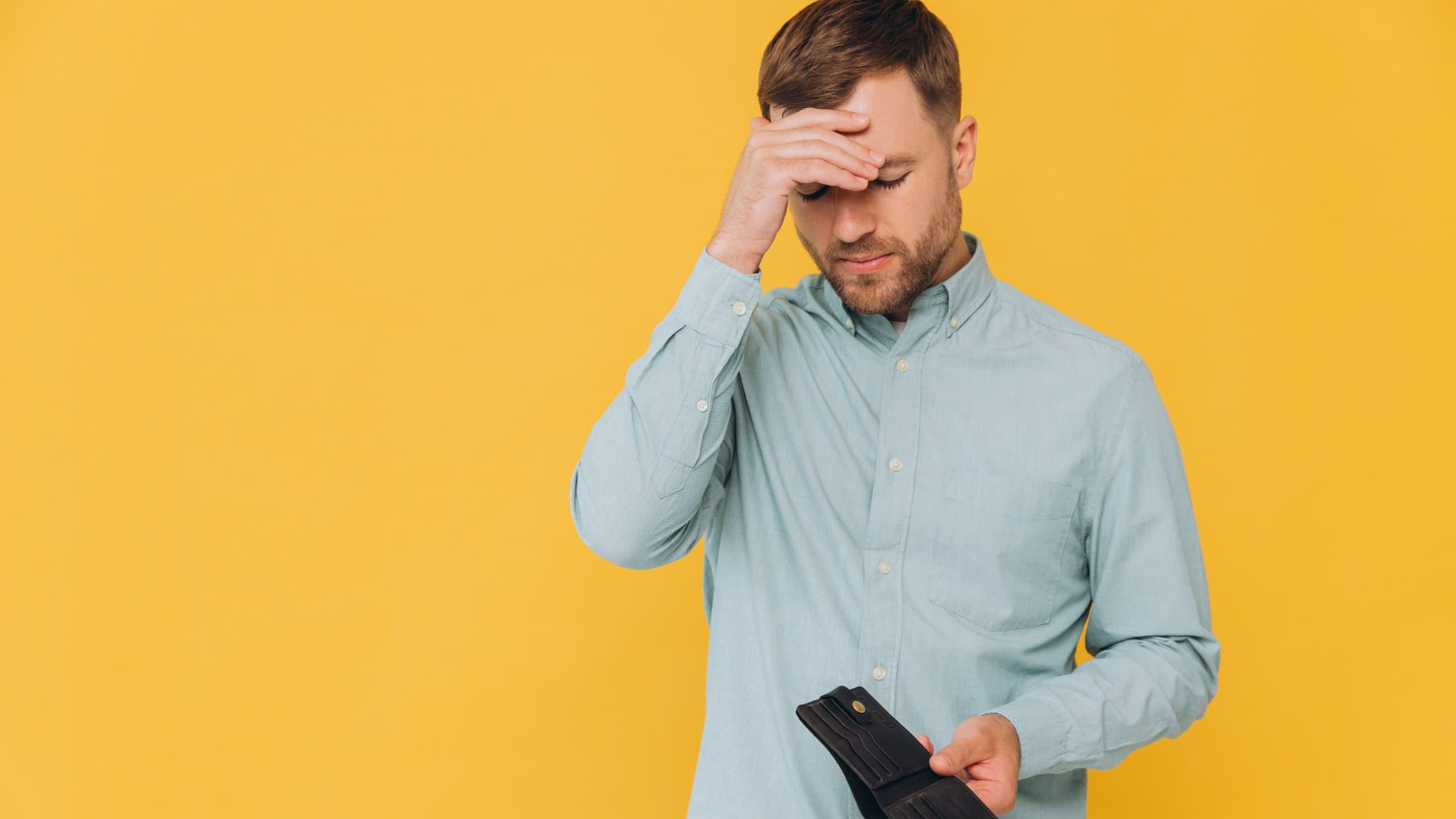 I'm Broke. Portrait of sad unshaven male bankrupt showing his empty wallet looking at camera. Upset man standing isolated over yellow studio background. Poverty Concept. Lack of money