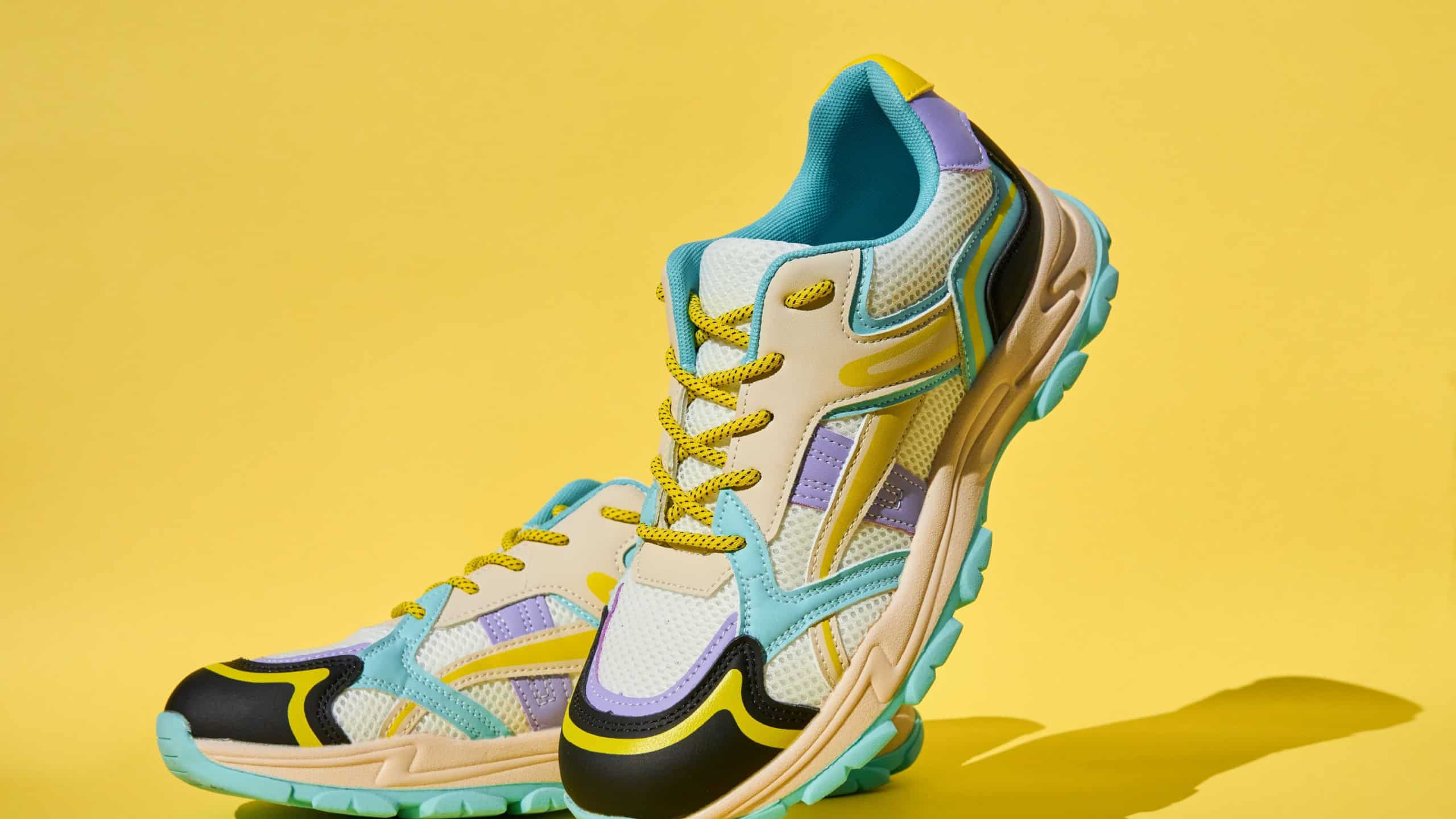 White sneakers with colored accents on yellow background, Pair of fashionable sport shoes. Studio shot of shoes for shop advertisement, creative minimalist style