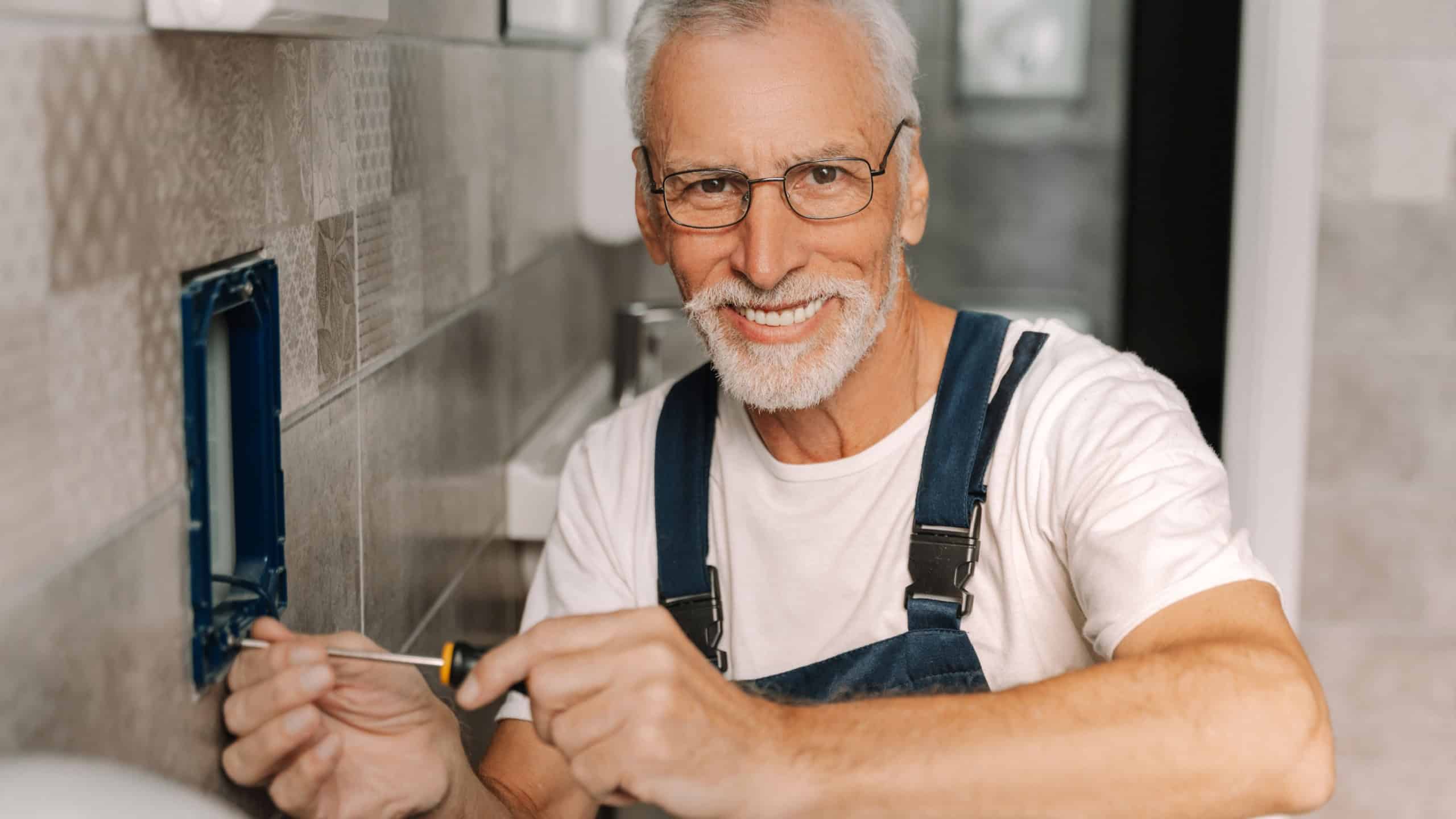 Experienced electrician happily installs power outlet in bathroom, confidently holding screwdriver, ensuring safety in home undergoing renovation