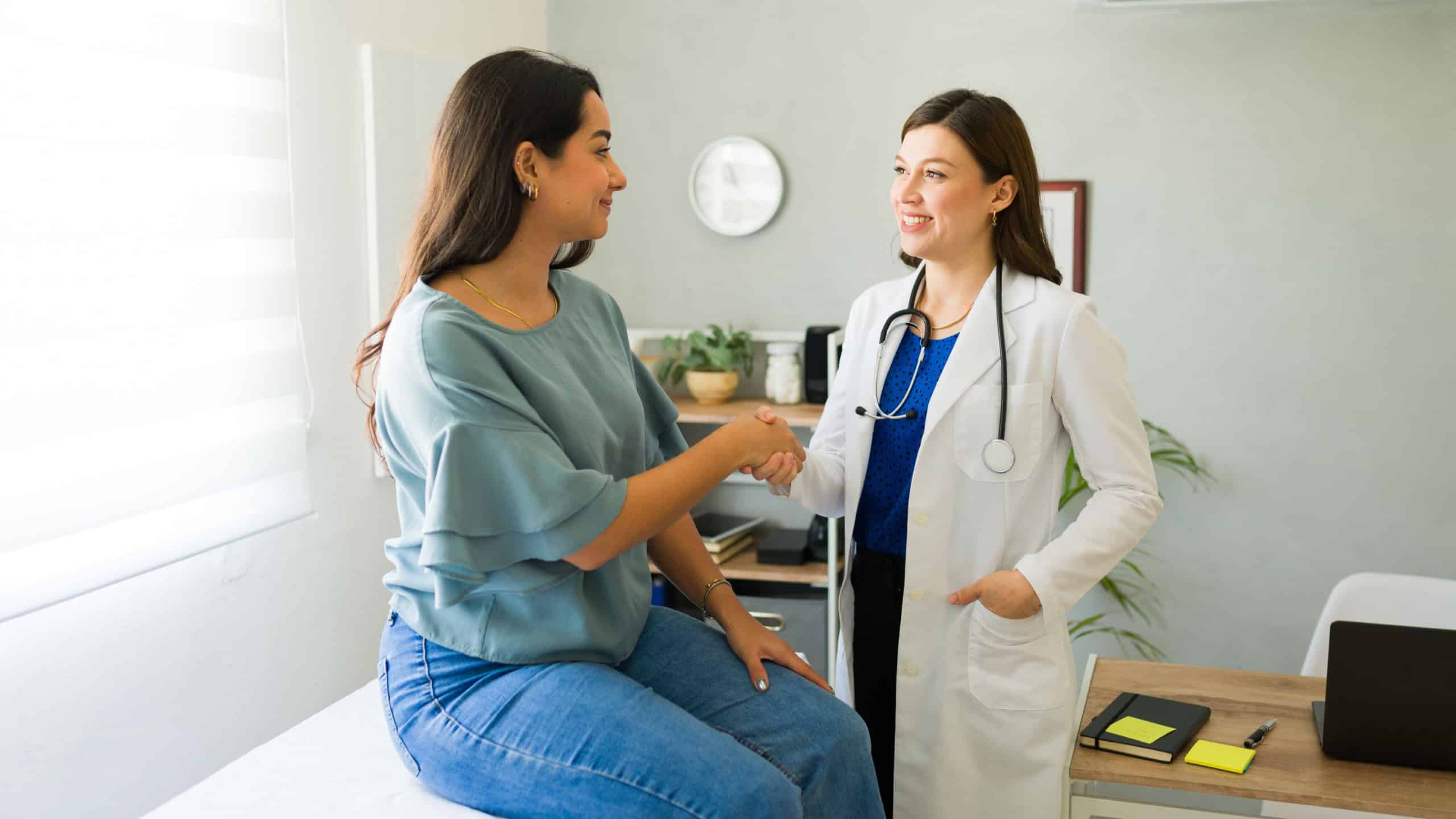 Female doctor happily shaking hands with her hispanic patient after a successful consultation in her office