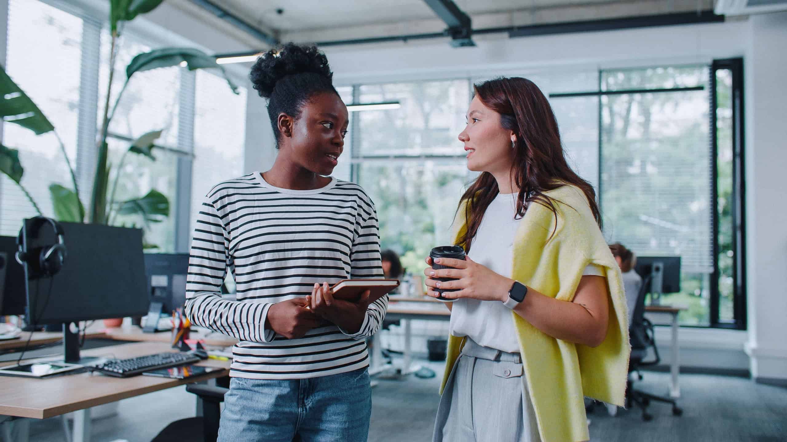 Multi-ethnic women talking together in modern office. Workers spending together coffee break. Having relaxed and friendly conversation. Colleagues discussing about planning time after work.