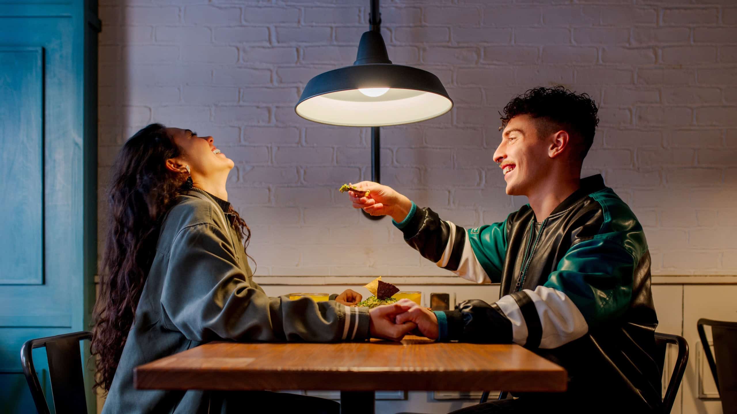 young Caucasian man offers food to his girlfriend as they dine together in a restaurant on a date. Boyfriend and girlfriend having a good time together.