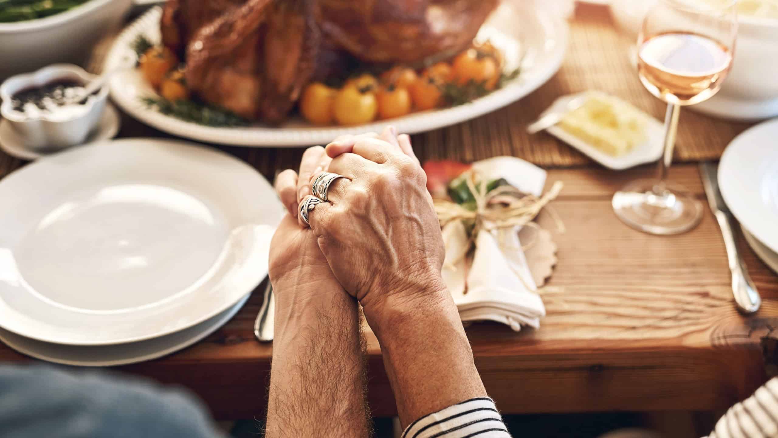 Hands, pray and food with a senior couple sitting at a dining room table for a roast lunch together. Prayer, grace and holding hands with a mature man and woman eating, bonding or enjoying a meal