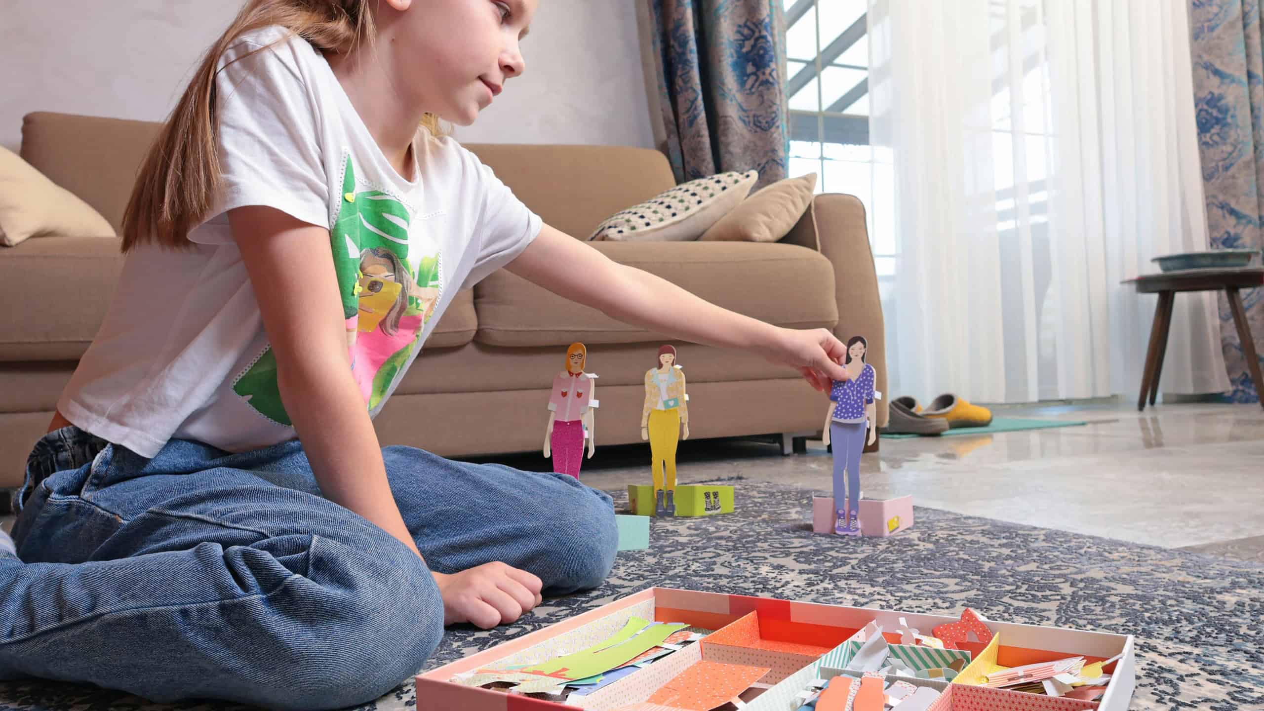 Teenage girl dresses up paper doll in room. Fashion and design. Pastime and lifestyle.