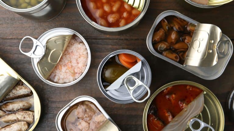 Open tin cans with different preserved products on wooden table, flat lay