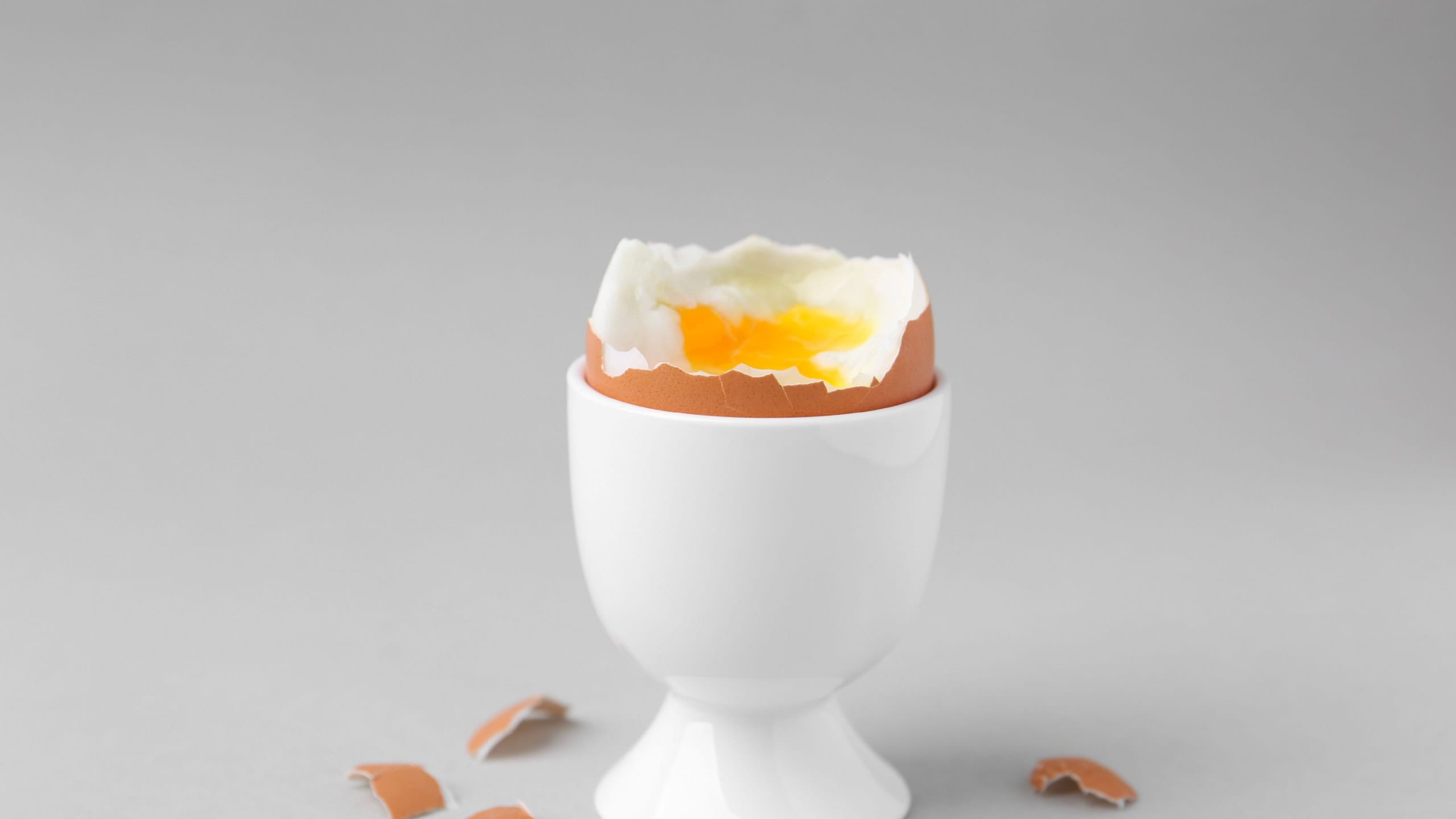 Soft boiled egg in cup and eggshell on light grey background