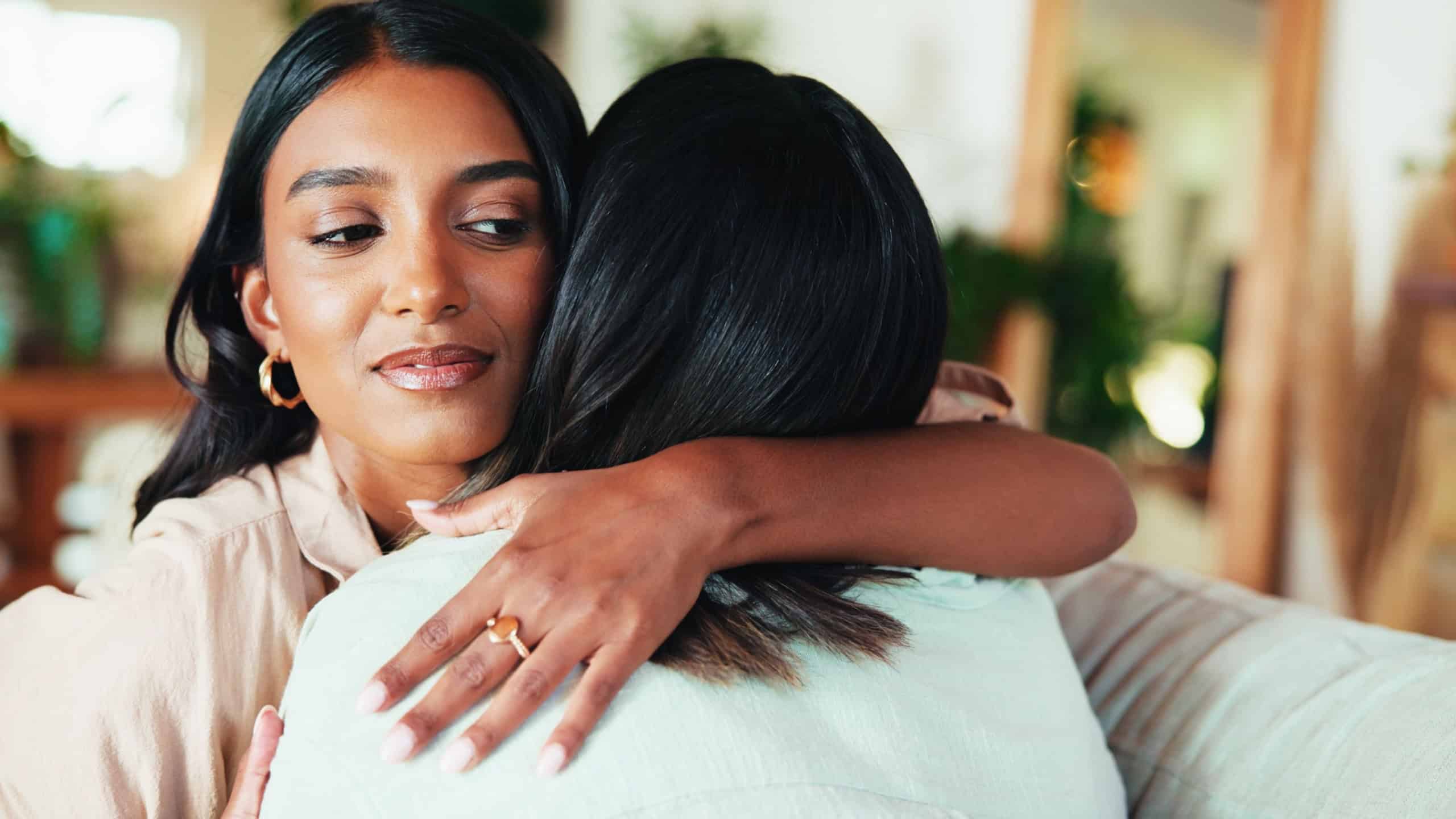 Fake, friends or women hug in house living room on sofa together with deceit, dishonesty or betrayal. Toxic, manipulation or people in home with embrace, jealous liar or trap for backstabbing or hate