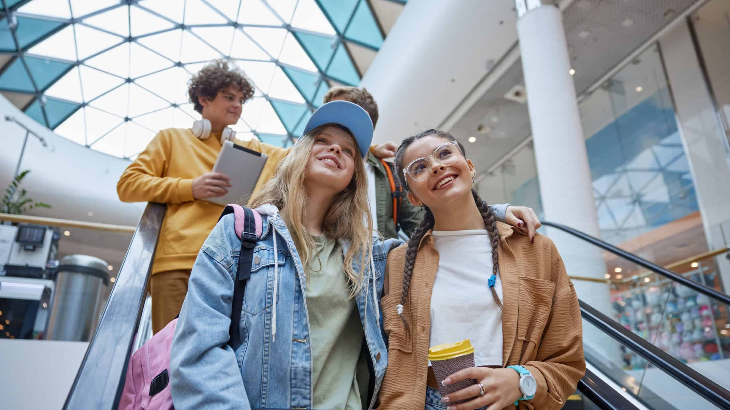 Happy carefree teenagers group riding escalator in shopping mall