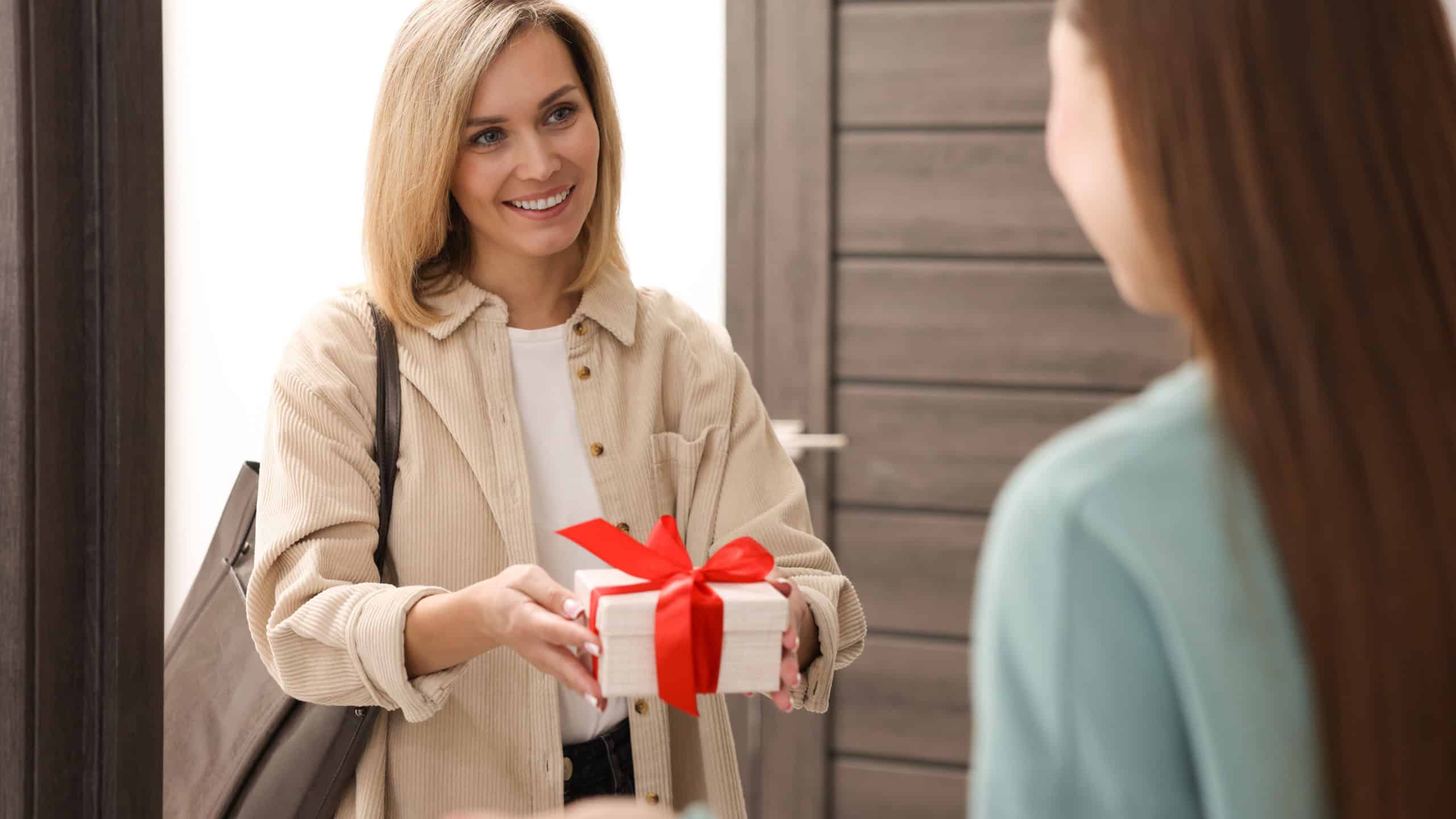 Woman giving housewarming gift to her friend at new apartment