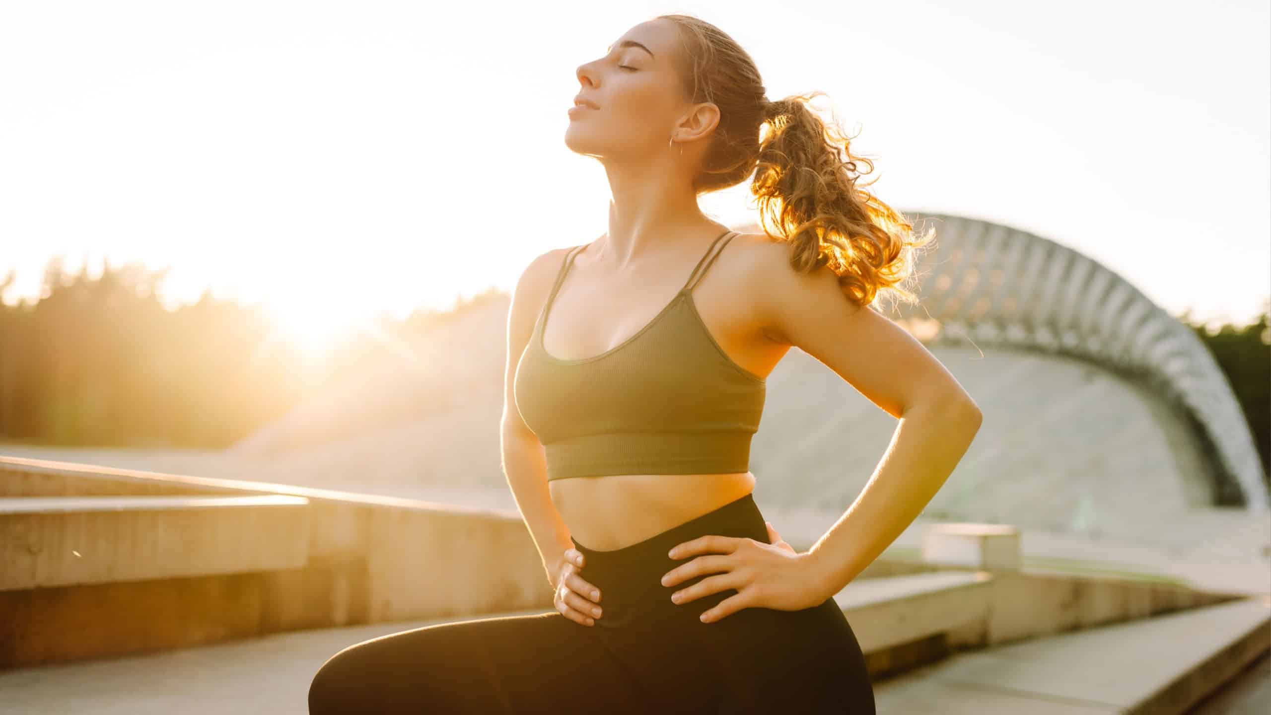 Sporty woman doing exercises at sunset. Beautiful woman in sportswear enjoying workout and feeling strong outdoors. Sports and fitness concept. Active lifestyle.