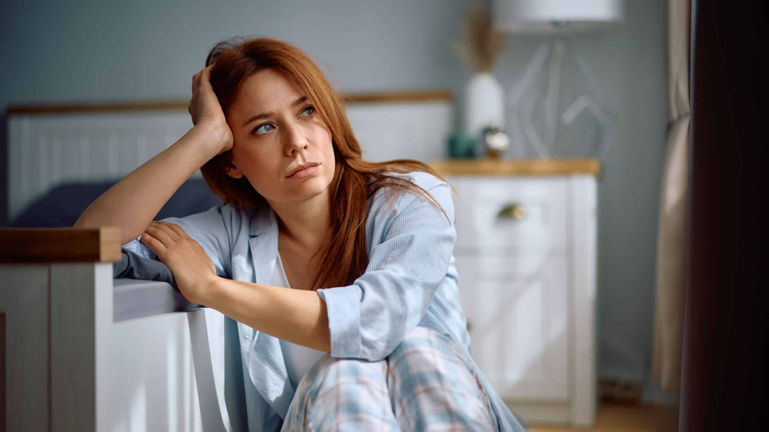 Pensive woman thinking of her problems while sitting in her bedroom.