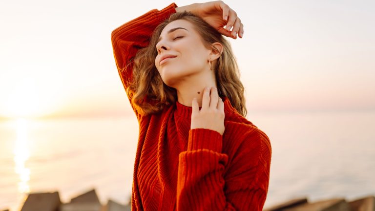 Beautiful woman smiling and walking on pier with seascape in background. Young woman enjoying sunset and feeling freedom. Walking concept, freedom. Active lifestyle.